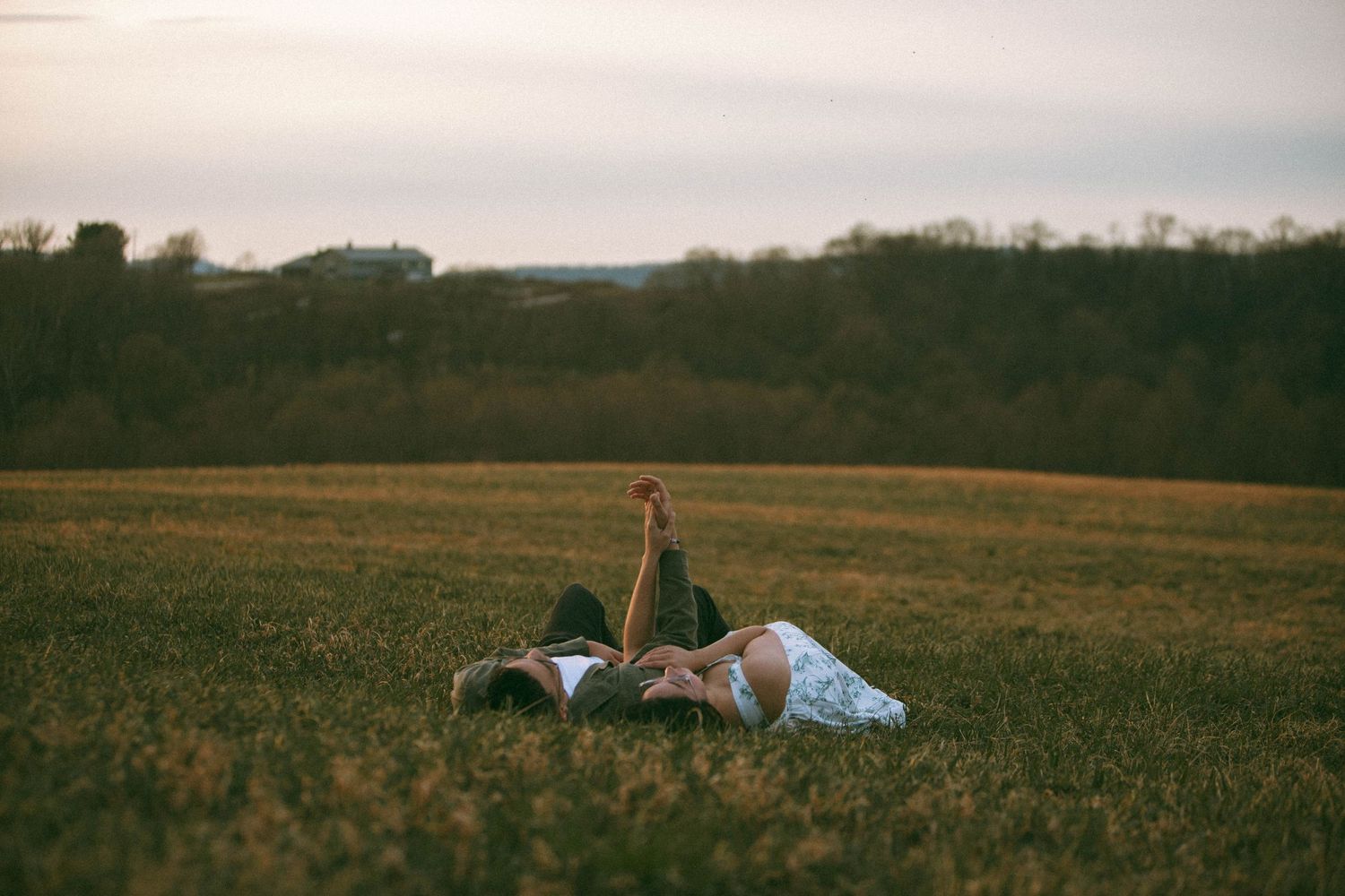 Couple lying on their back in grassy field at sunset with treeline in background for a couples session by Lancaster Photographer