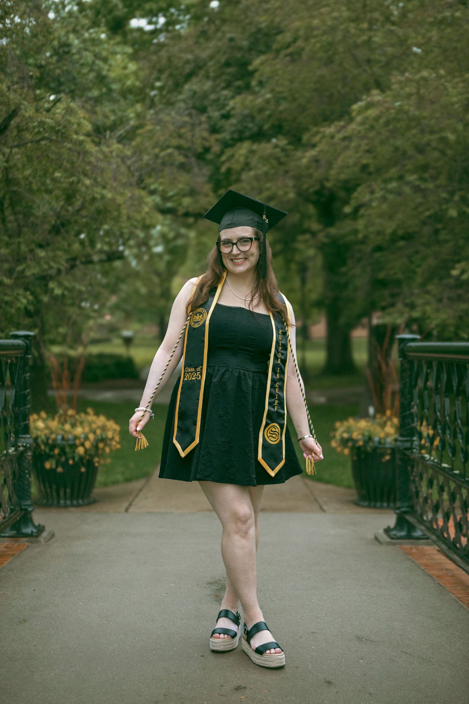 Outdoor graduation session by D'Gallery at the Millersville University campus, surrounded by greenery and flowers on a bridge over a pond.