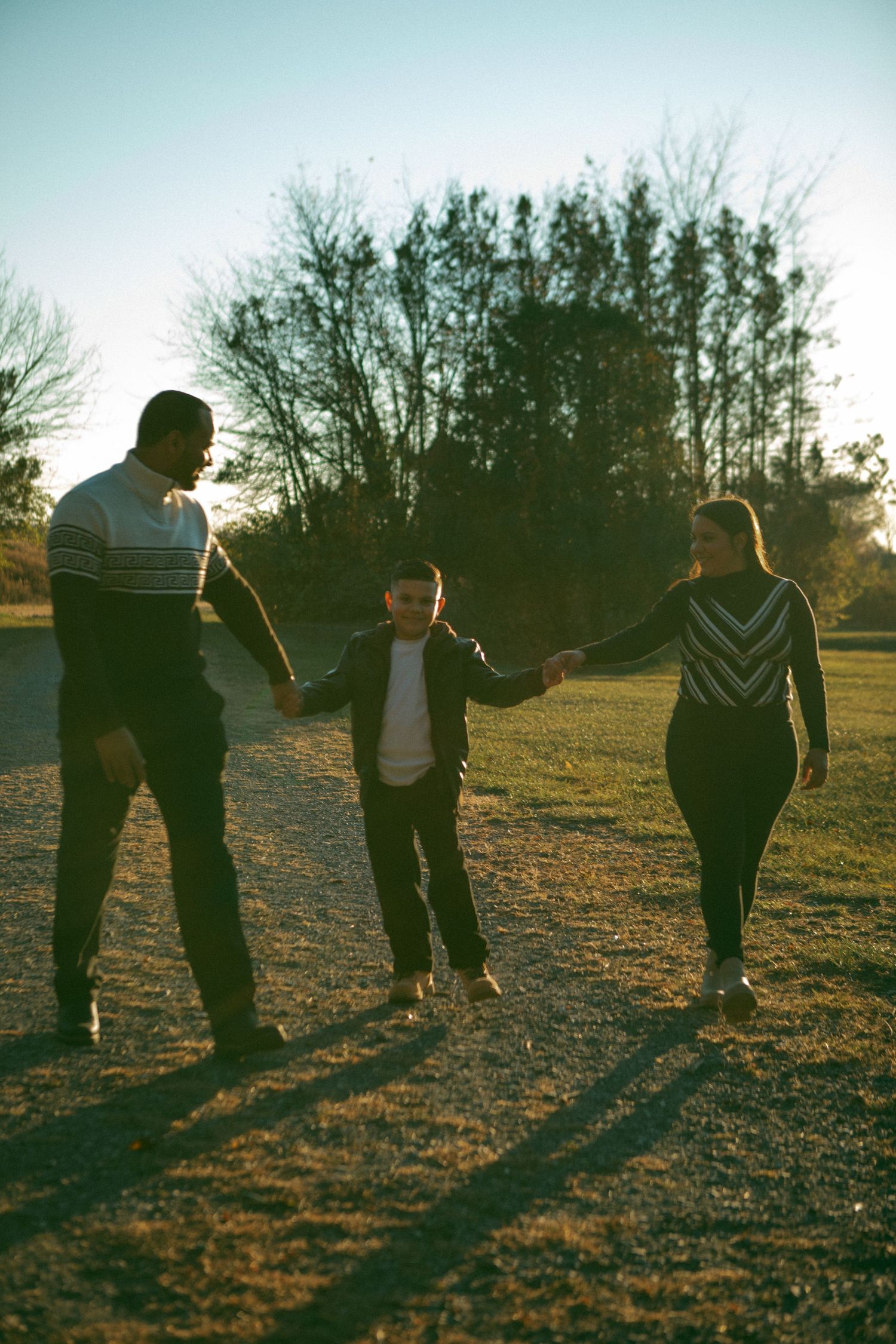 A family walks hand in hand along a sunlit path, their shadows stretching in the golden evening light.