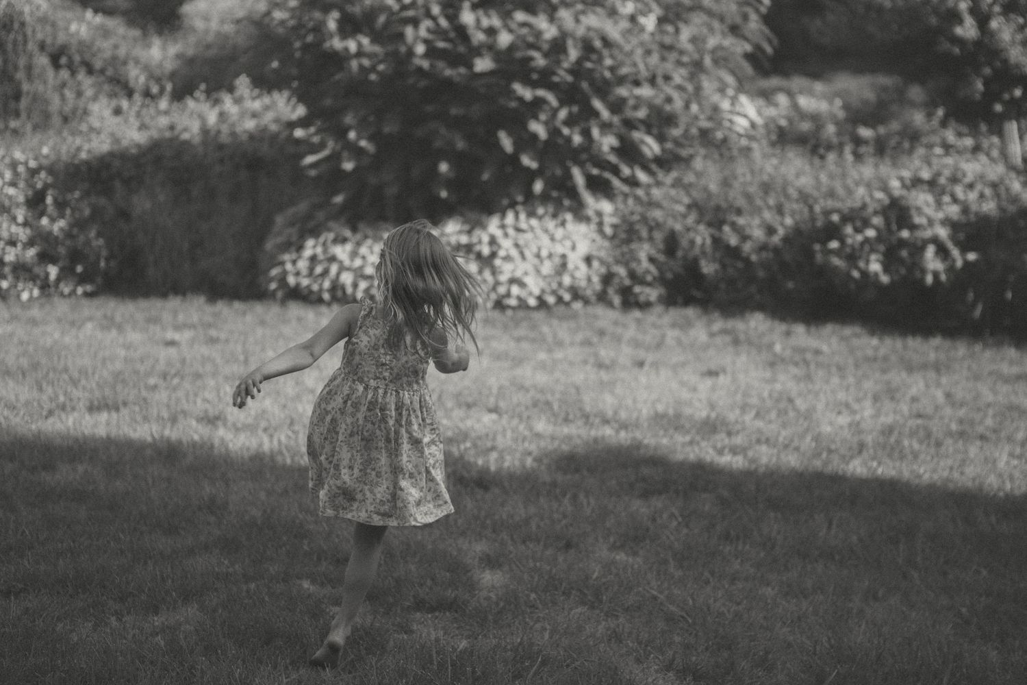 During a senior session, a little girl runs gracefully on a grassy lawn at Longwood Gardens in a dreamy black and white photograph