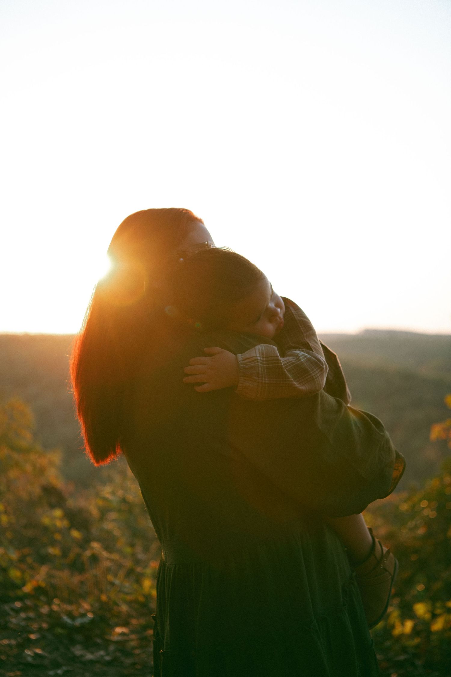 Mother and child embracing at sunset, bathed in warm golden light, symbolizing love, warmth, and a deep family bond.