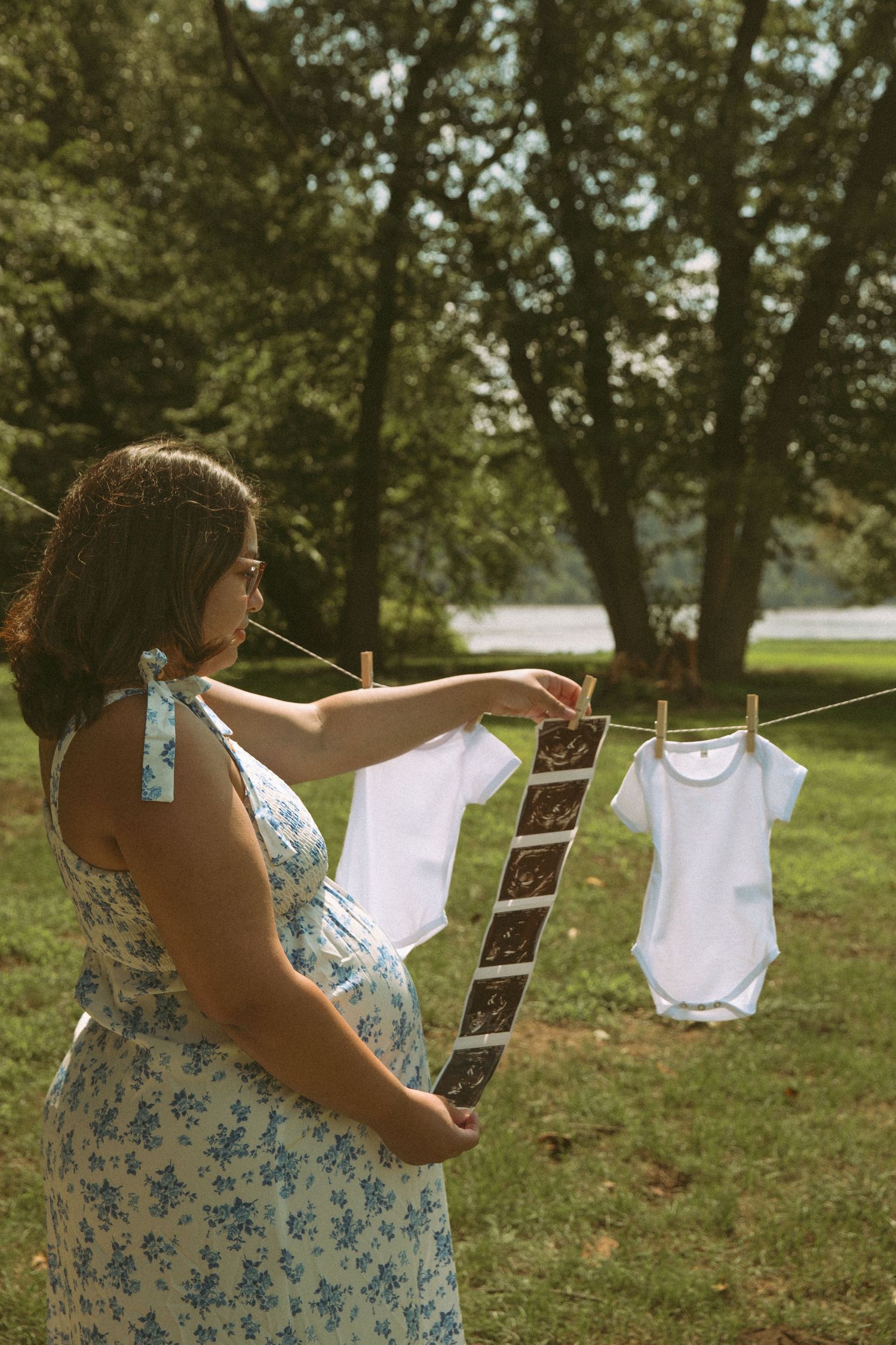 Pregnant woman holding ultrasound photos near baby onesies on a clothesline, symbolizing anticipation, motherhood, and the joy of expecting.