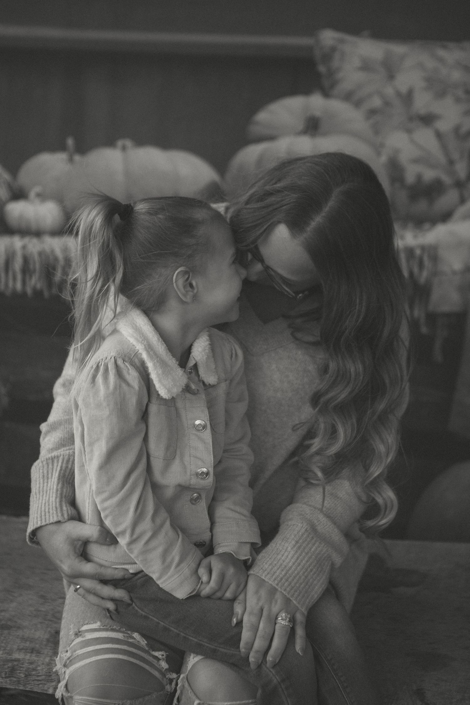A mother and daughter share a sweet, nose-to-nose moment, radiating warmth and love in a cozy autumn setting.