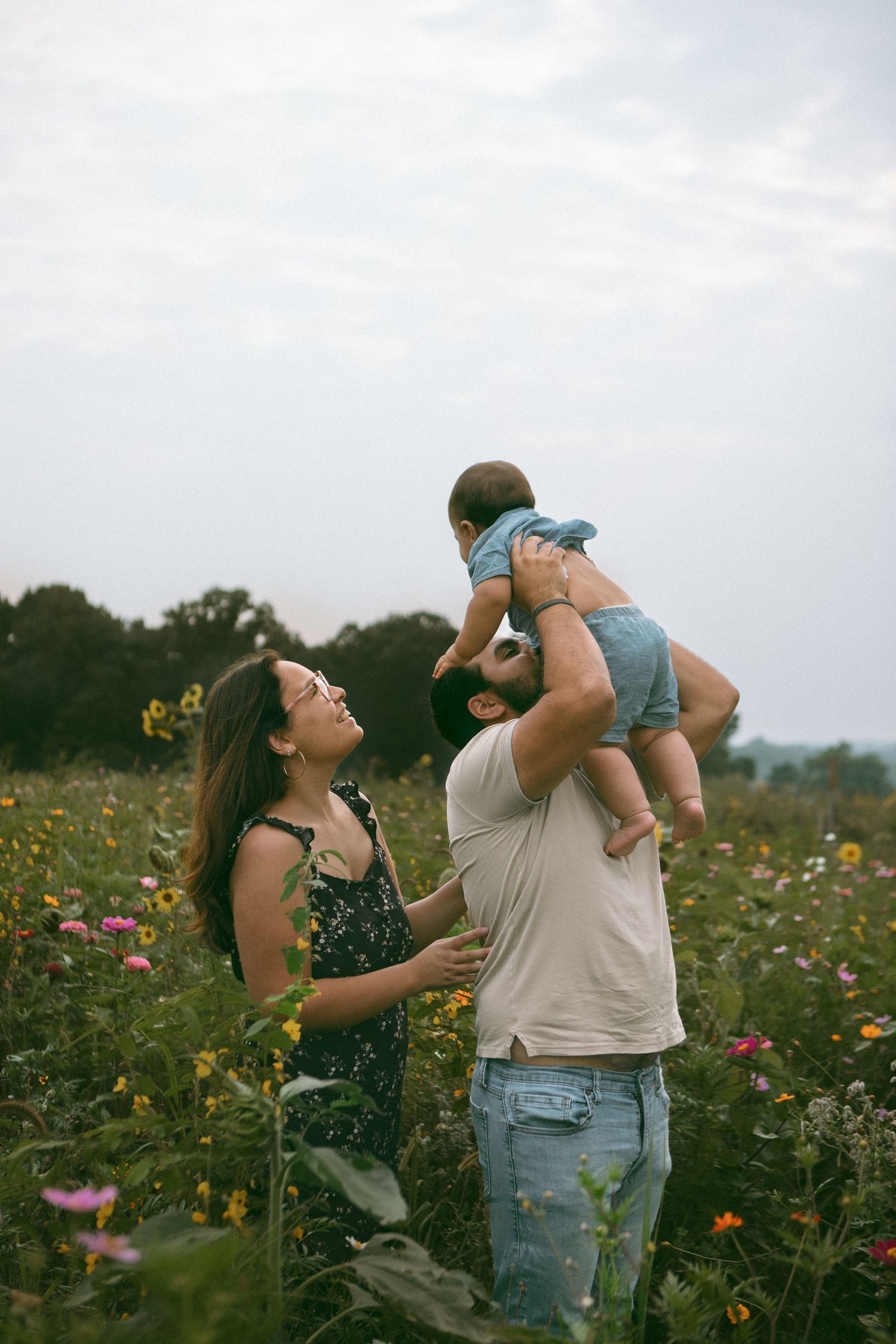 A couple plays together in a vibrant wildflower field during golden hour, lifting their baby up playfully during a family photo shoot.