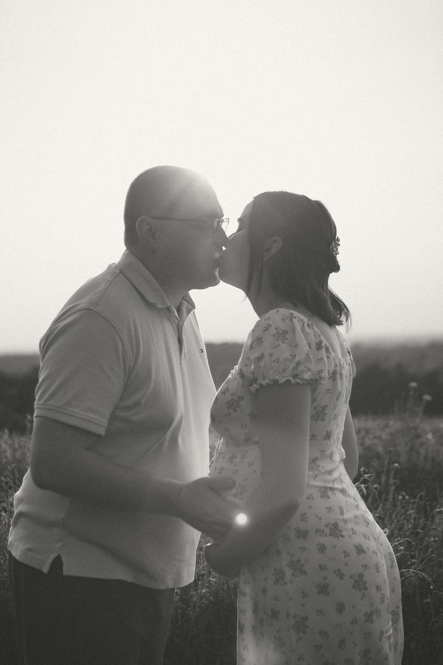 A romantic couple embraces in a field during sunset in a black and white photograph by D'Gallery Photography in Ronks, PA.