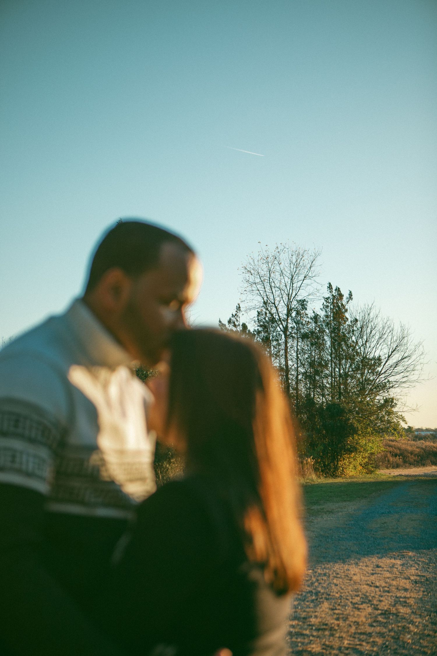 Romantic couple shares a tender moment at sunset, with a man kissing a woman's forehead in a blurred outdoor family session in Lancaster, PA