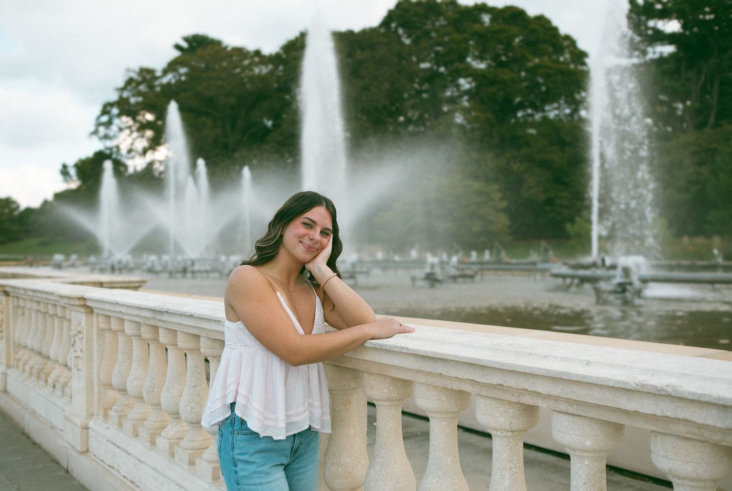 A young woman enjoys a peaceful moment by a grand fountain, leaning against the stone railing with a soft smile.