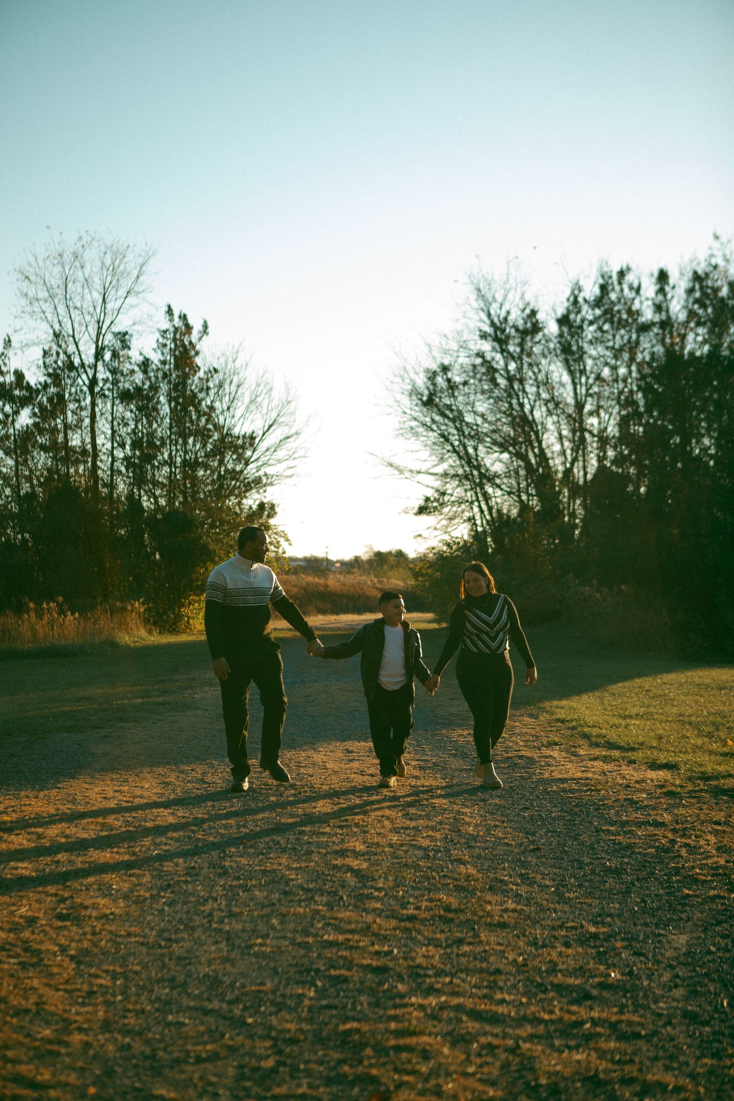 A family walks hand in hand along a sunlit path at sunset, surrounded by nature, creating a warm and loving moment of togetherness.