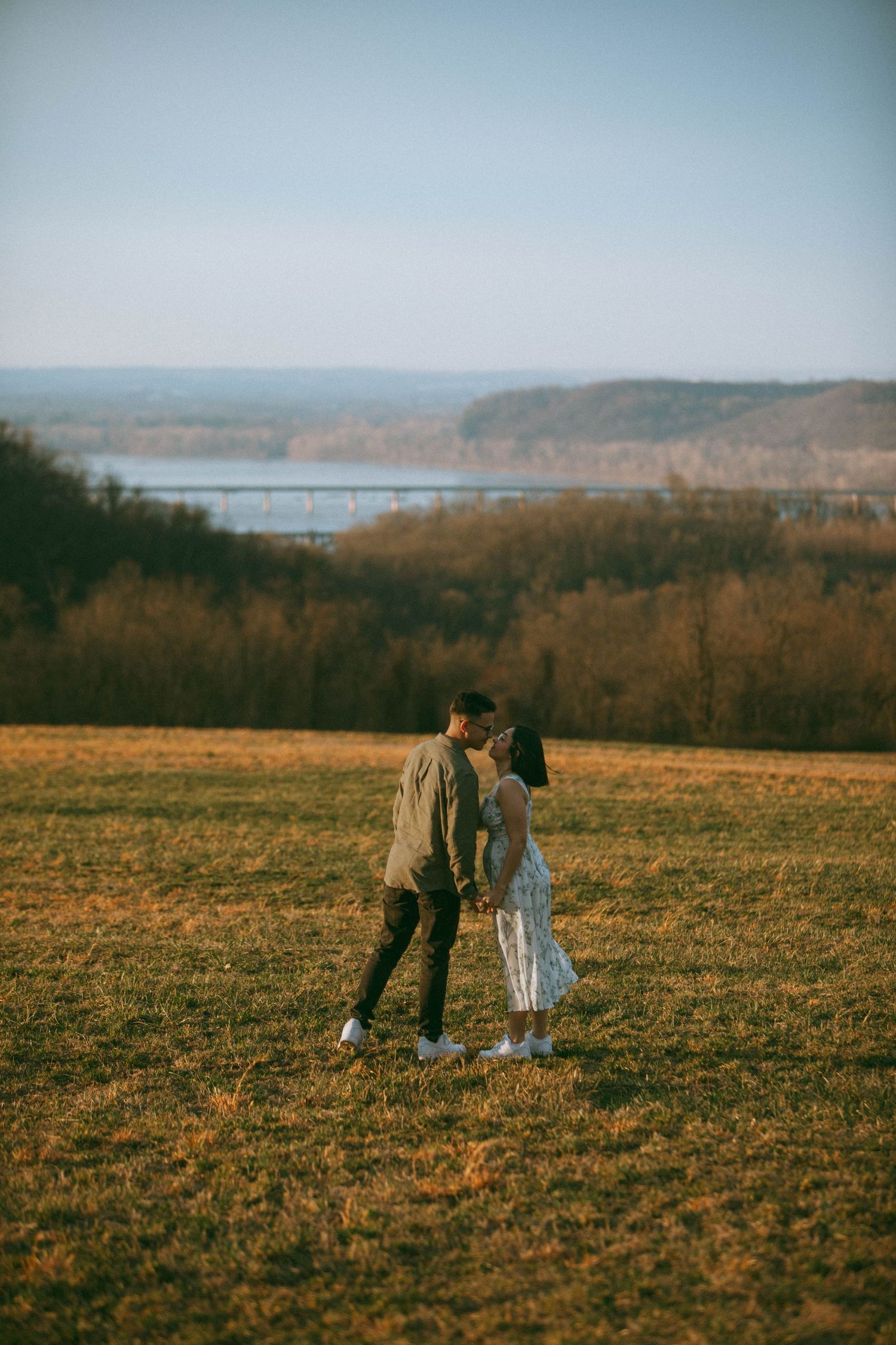 Couple in a golden field overlooking a scenic lake and hills during sunset hours by Storytelling Photographer in Lancaster, PA D'Gallery