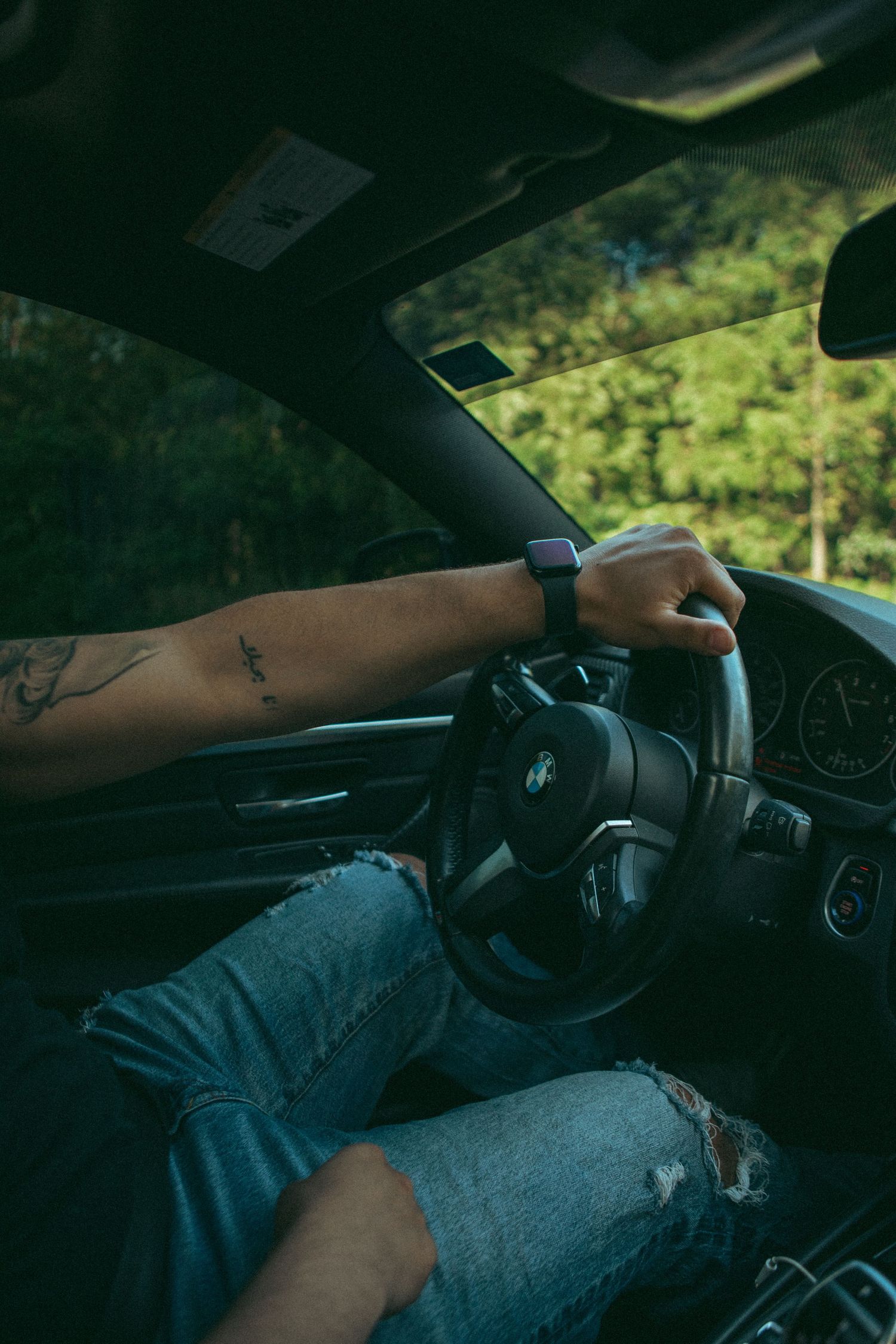 Moody car interior shot of a tattooed driver gripping a BMW steering wheel, capturing movement, style, and adventure. #AutomotivePhotography