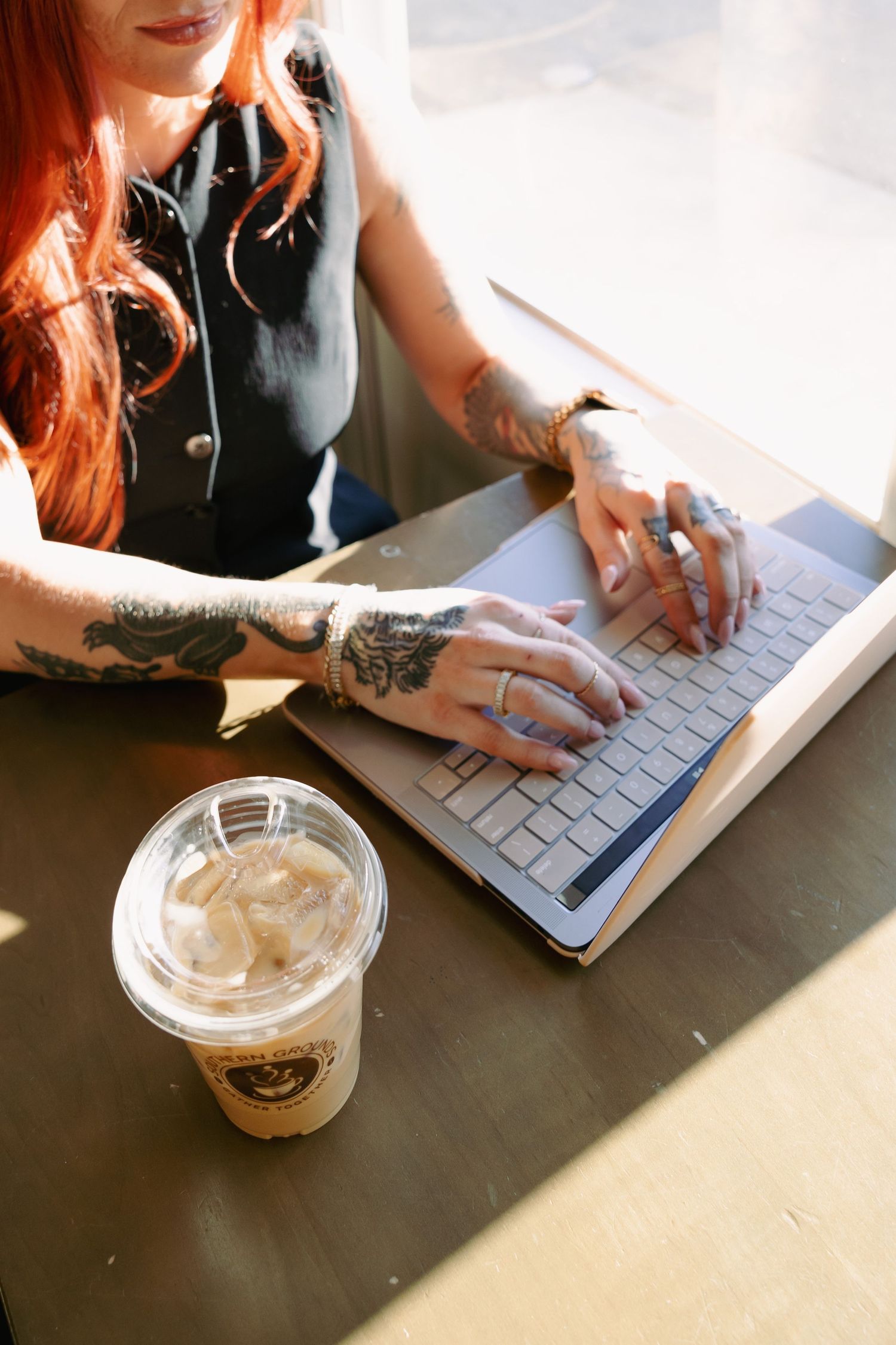 detail photo of coffee and laptop, with a woman typing on the keyboard