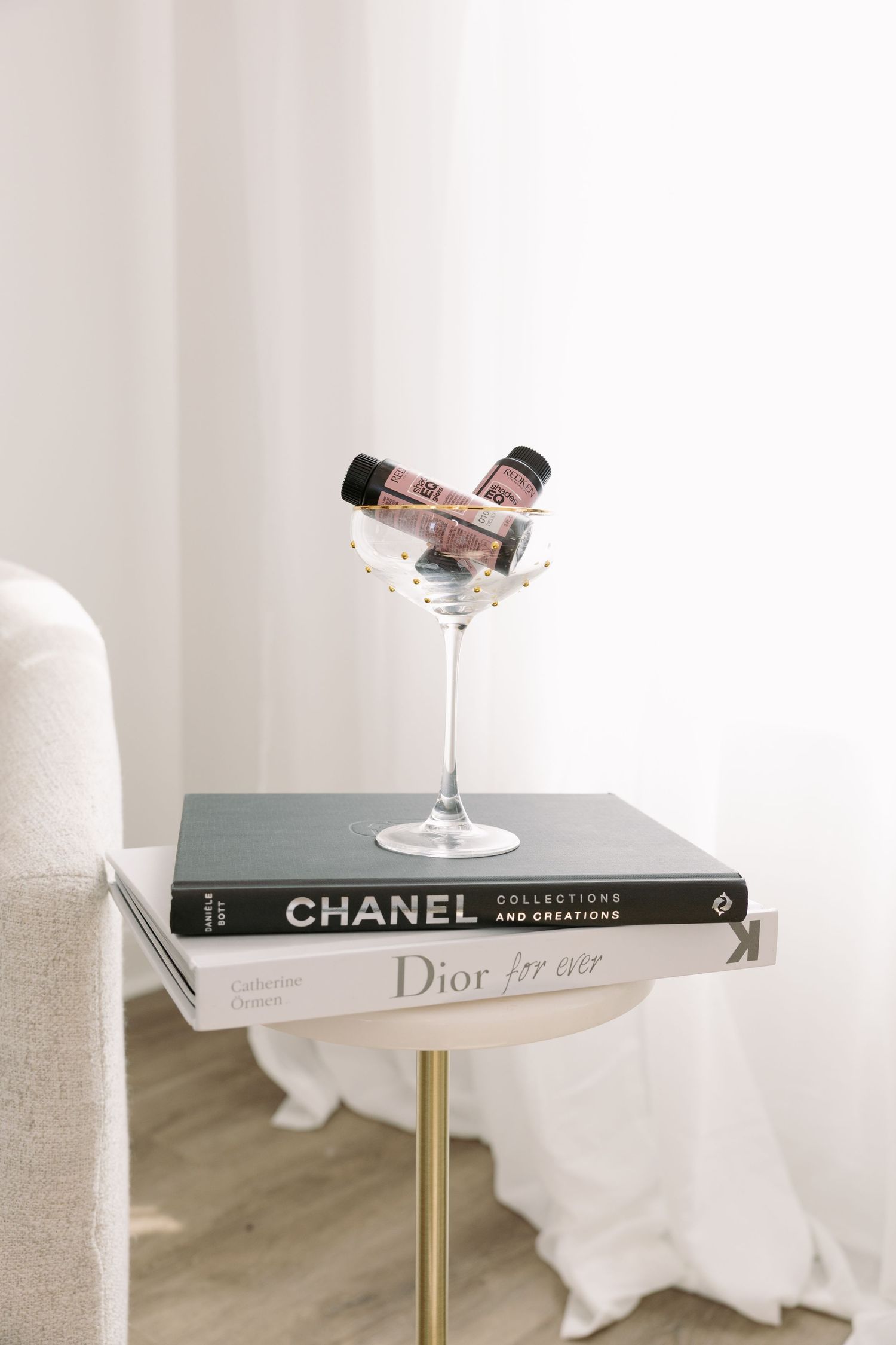 fashion books on side table featuring a hair product inside a martini glass.
