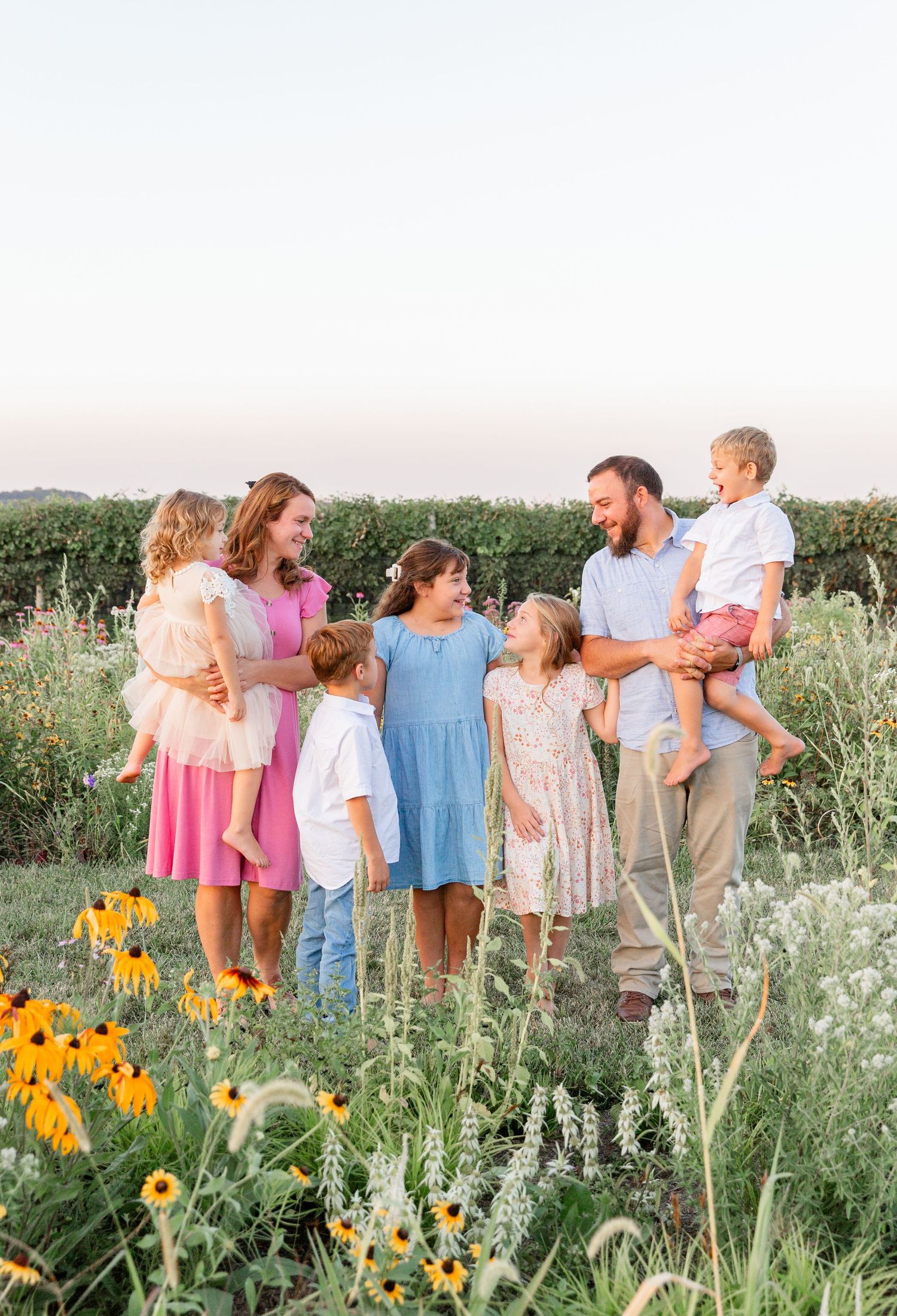 Family stands together in a wildflower meadow with orange flowers blooming at sunset during summertime.