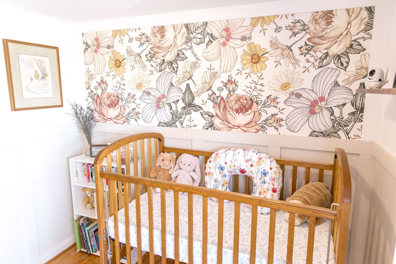 Vintage wooden crib with floral wallpaper backdrop and decorative pillows in a cozy nursery corner.
