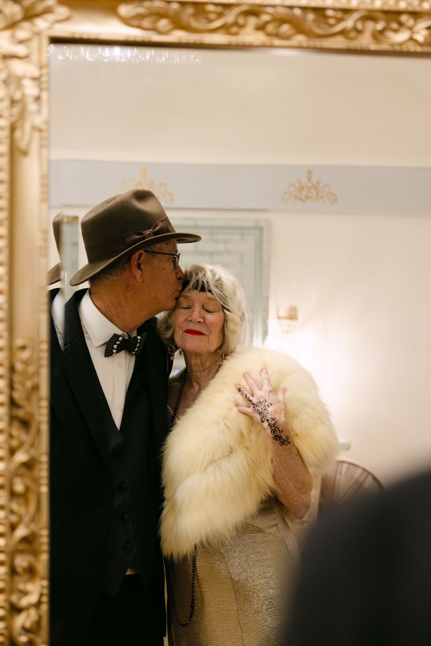 A couple shares an intimate moment at an elegant venue, with the person wearing a white fur stole and formal attire.