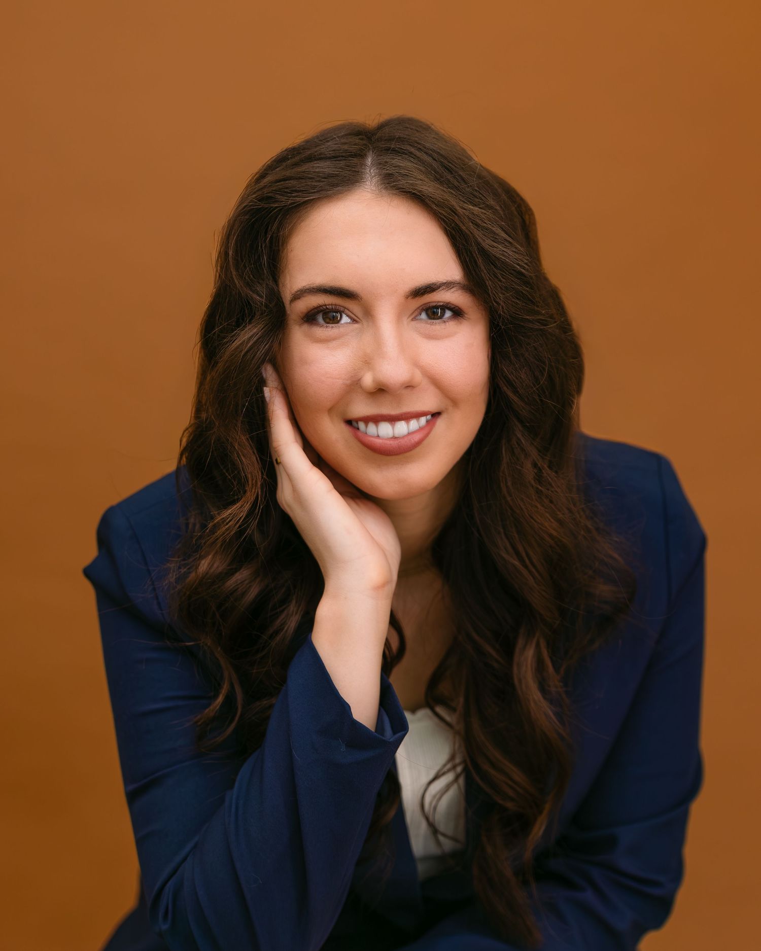 Professional portrait series of a person in a navy blazer against an orange background showing different expressions.