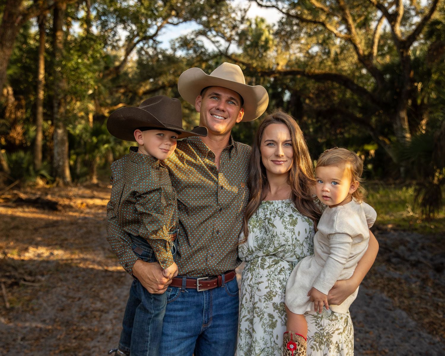 A family poses together outdoors in a wooded setting during golden hour lighting.