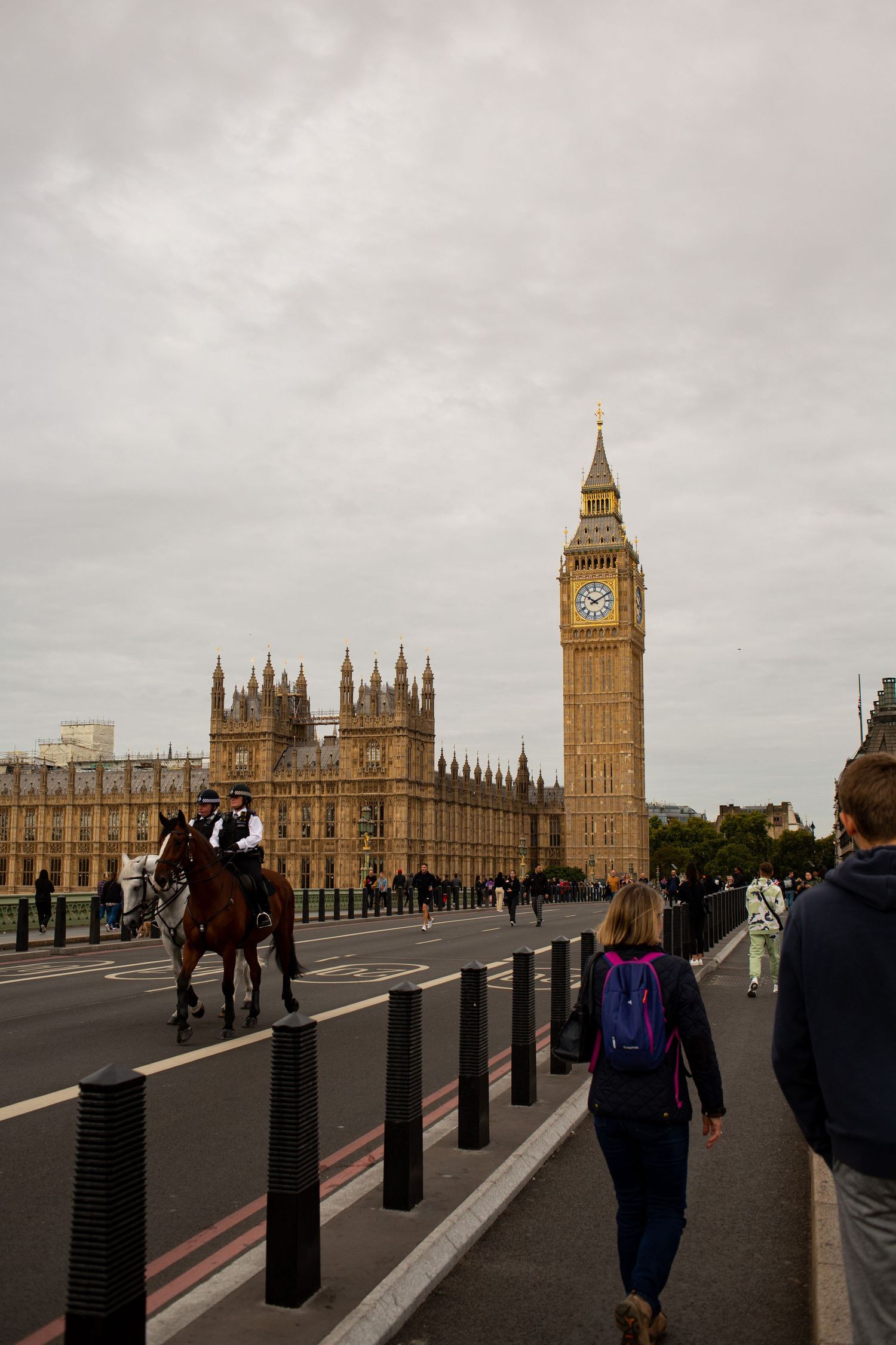 Mounted police officers patrol Westminster Bridge near Big Ben and Houses of Parliament on a cloudy London day.