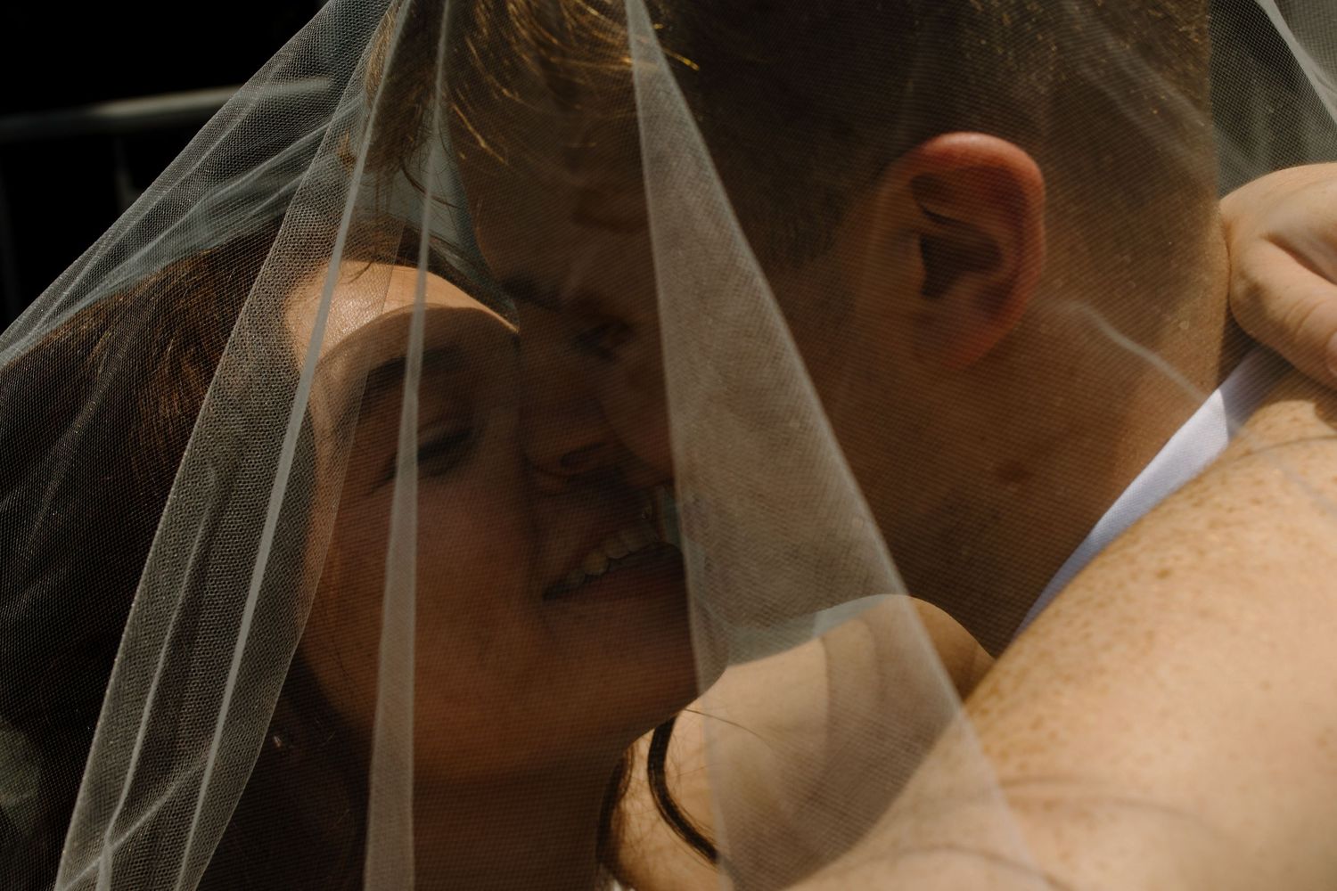 A romantic wedding moment captured through a delicate white veil as the couple shares a tender embrace.