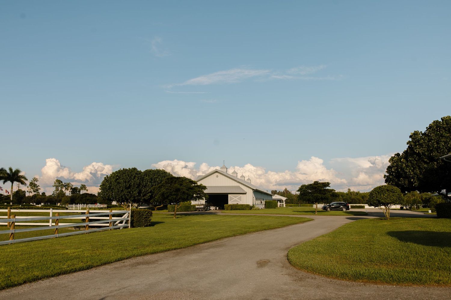A panoramic view of a winding country road through rolling green farmland under a bright blue summer sky.
