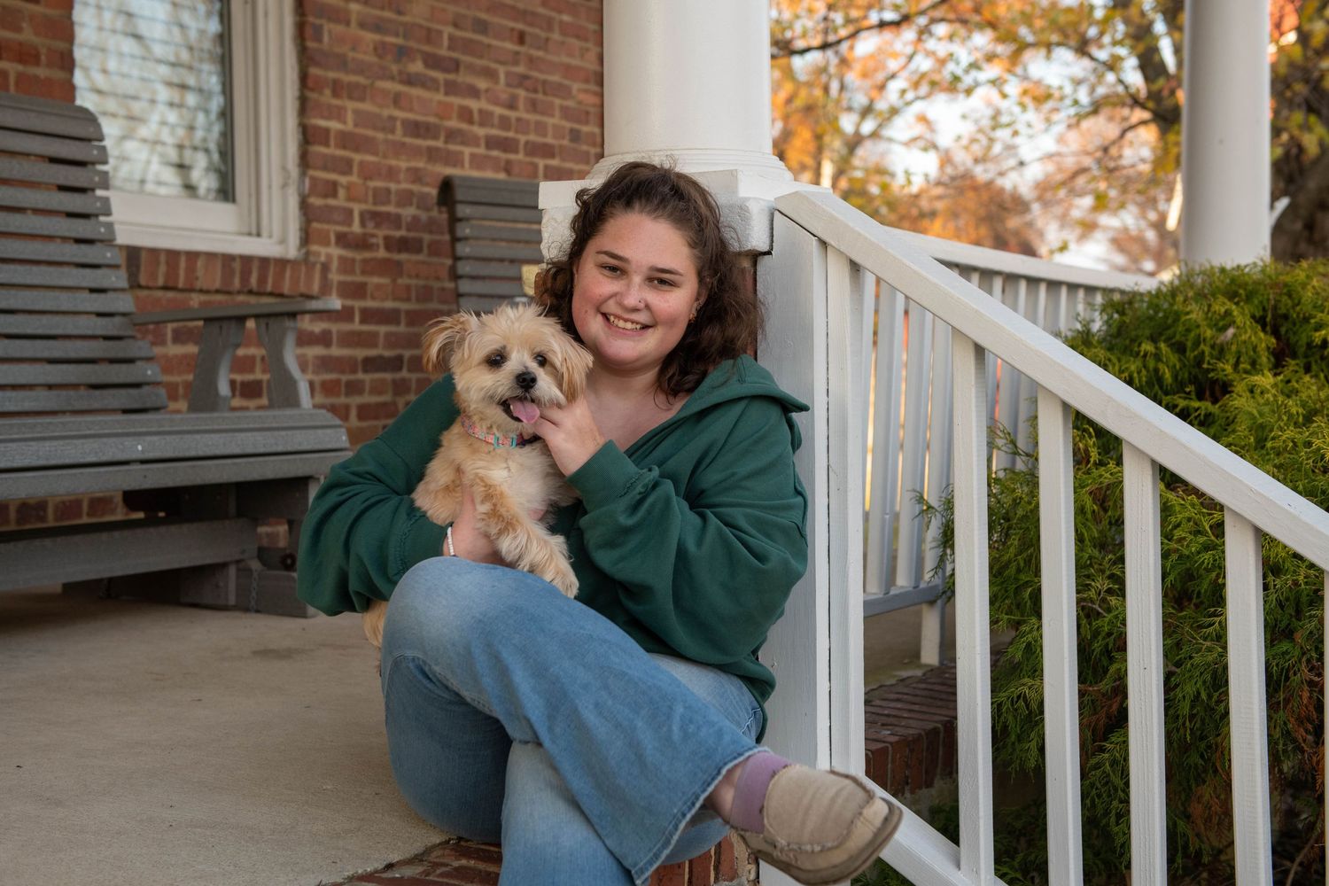 Someone sitting on a porch with a small fluffy dog on their lap.