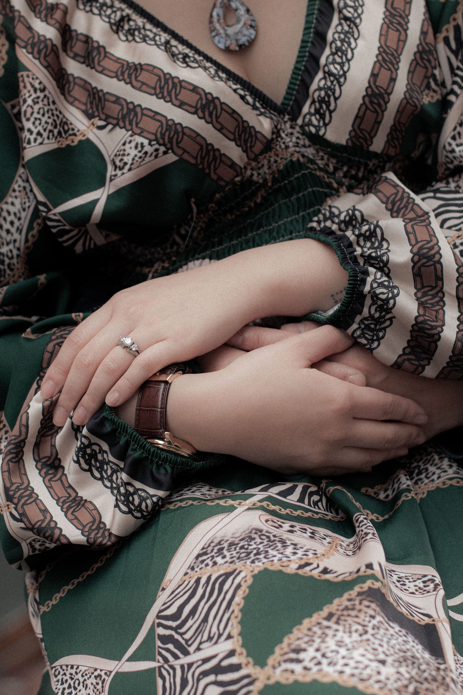 Close-up of woman's hands wearing a gold watch and diamond ring, dressed in elegant green patterned silk dress.