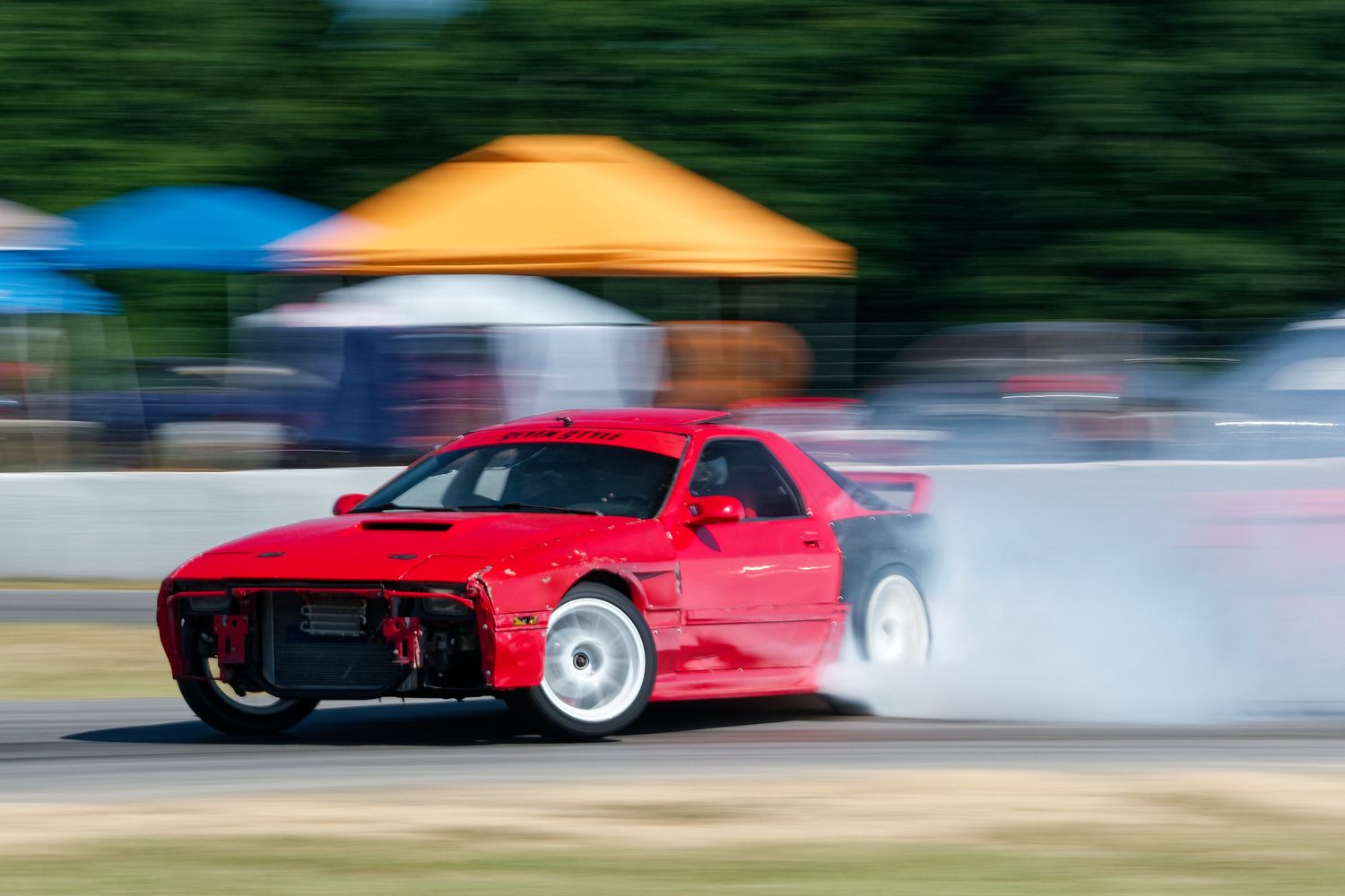 Red sports car drifting on a track with smoke billowing from the tires.