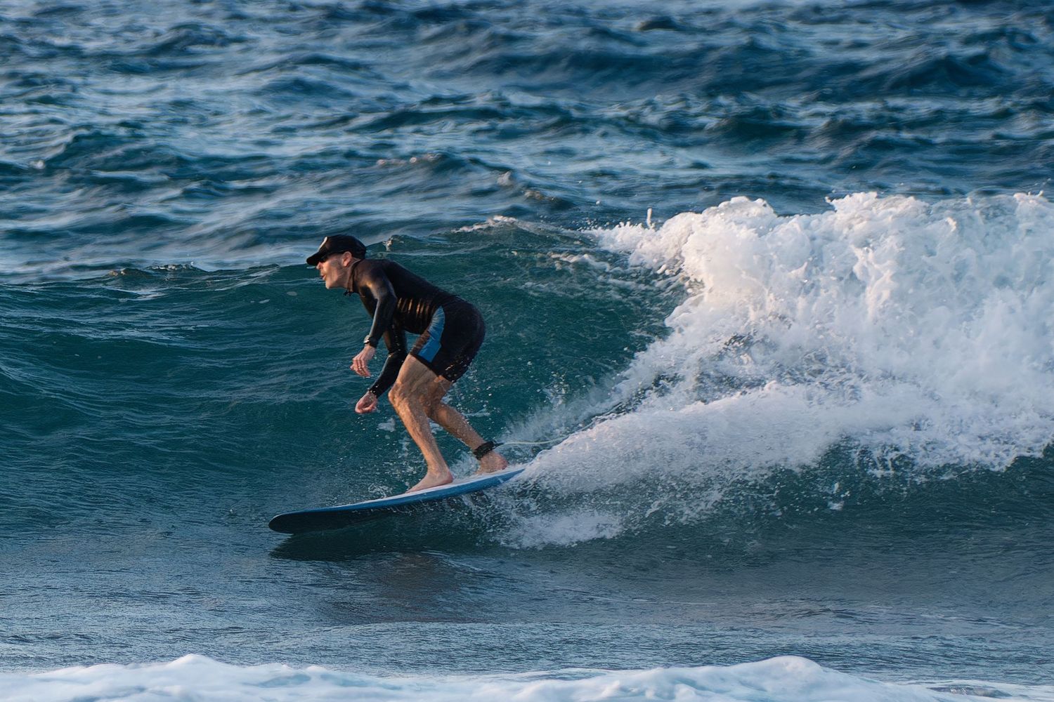 Surfer riding a breaking wave on blue ocean waters in dynamic action shot.