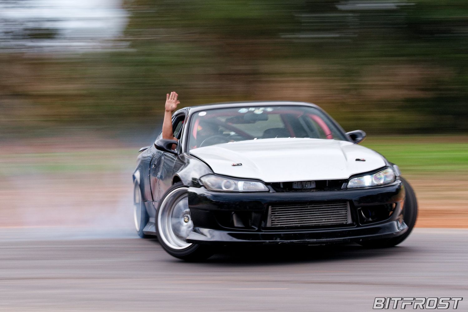 Modified black sports car drifting sideways on a wet track with motion blur effects.