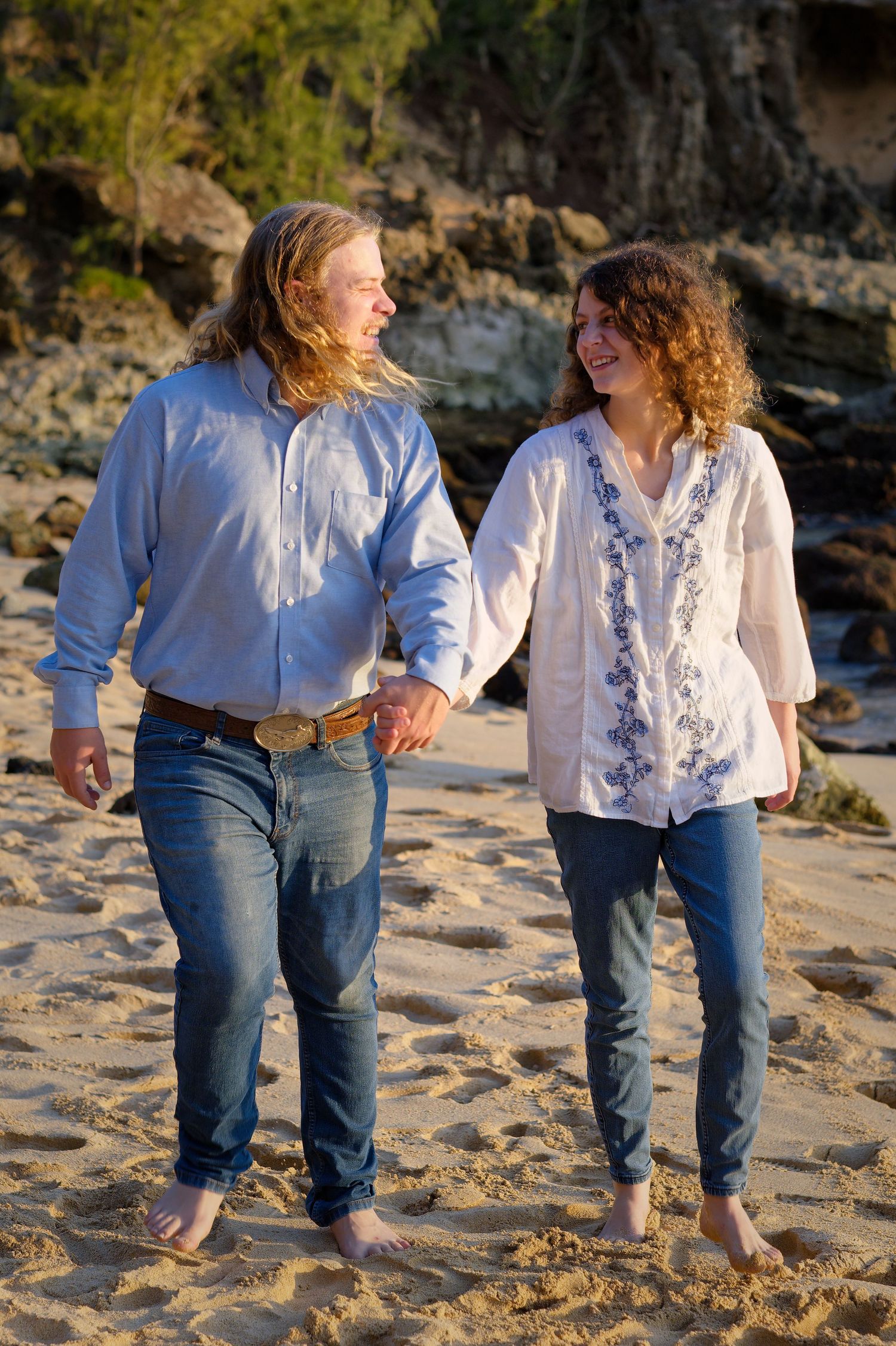 A couple walks barefoot along a scenic beach at sunset