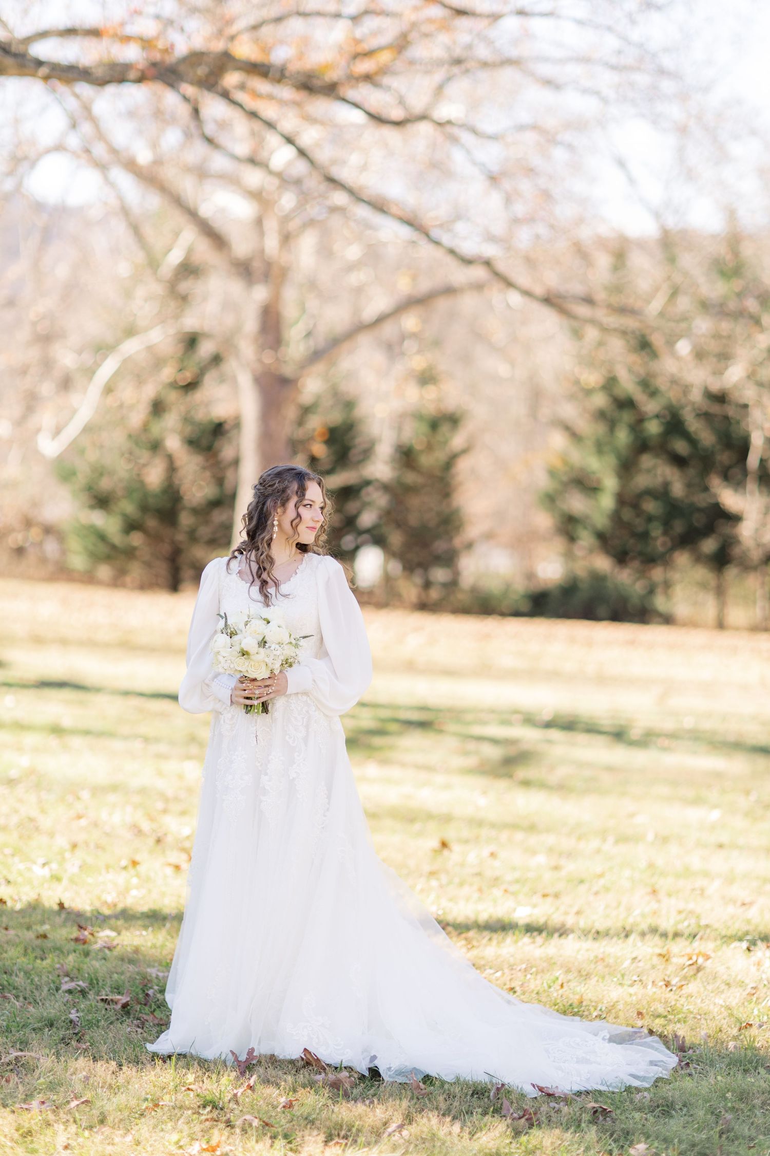 Ethereal bridal portrait in flowing white dress against autumn landscape.