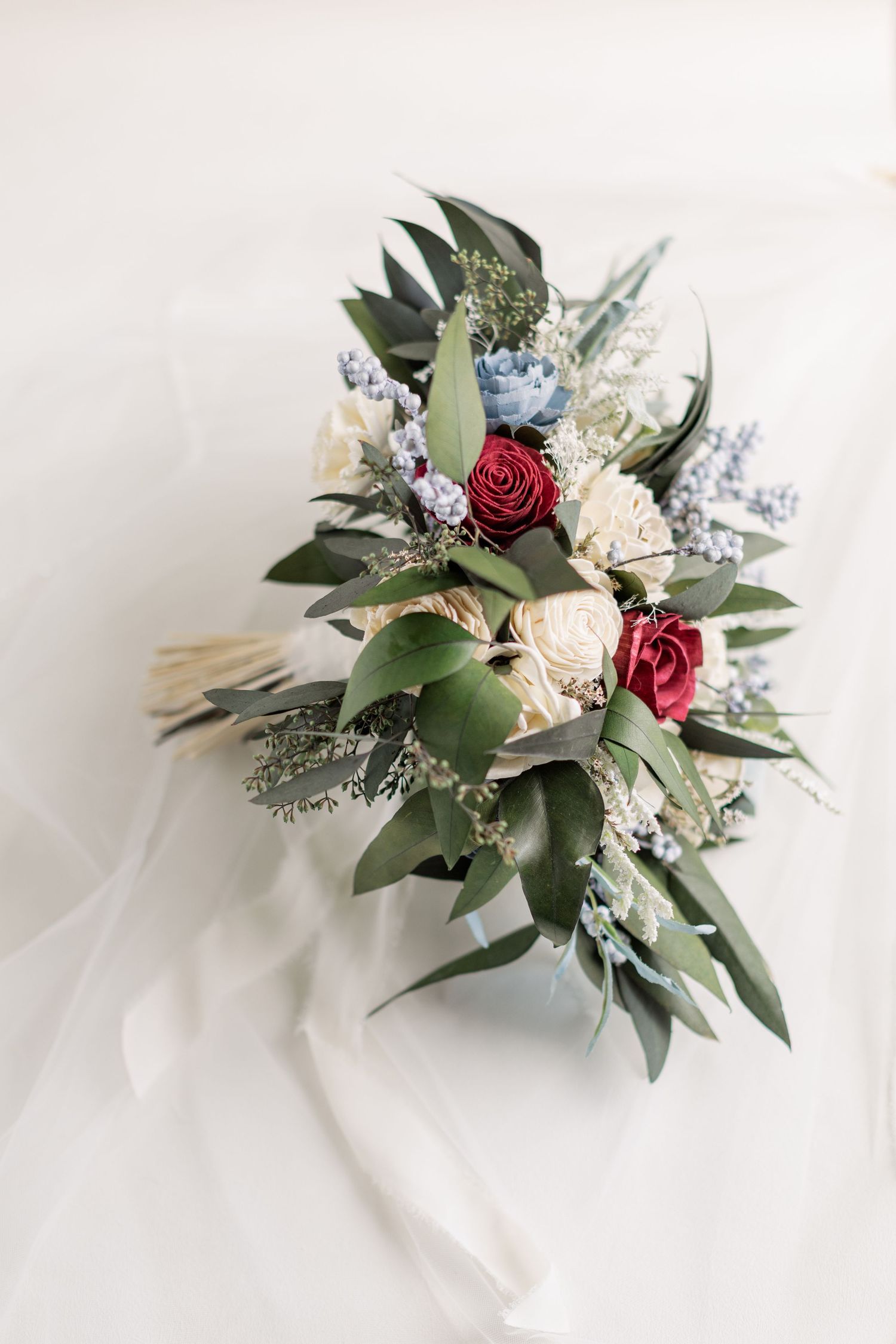 A wedding bouquet with red roses, white flowers and eucalyptus leaves on a light background.
