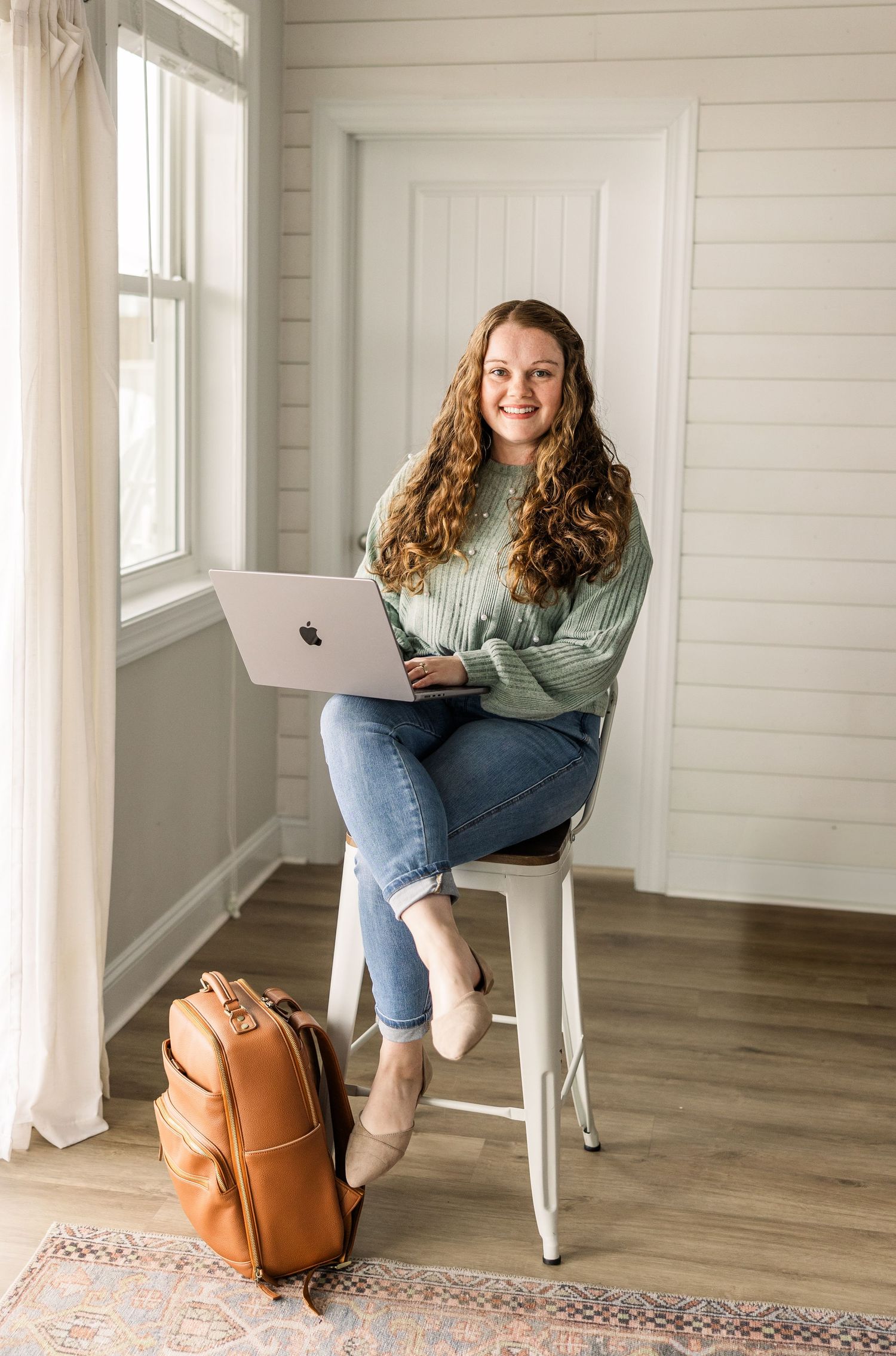 A casual workspace setup with a laptop and brown leather bag on a patterned rug.