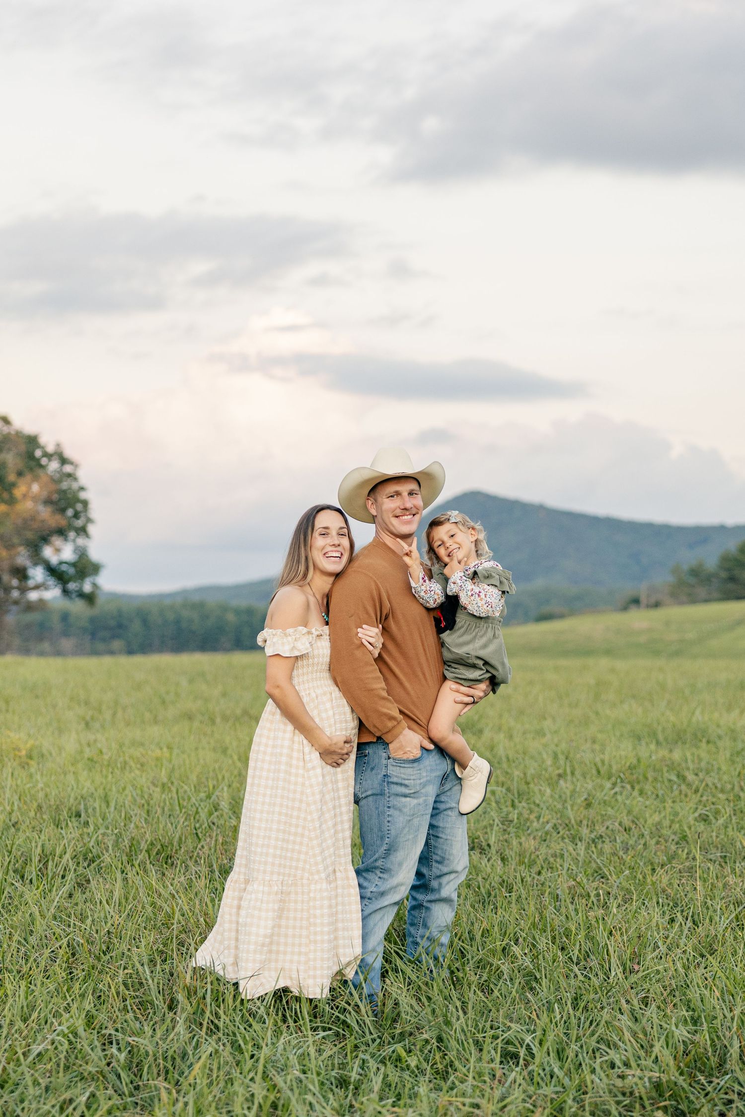 A family stands together in a grassy meadow with mountains in the background during golden hour.