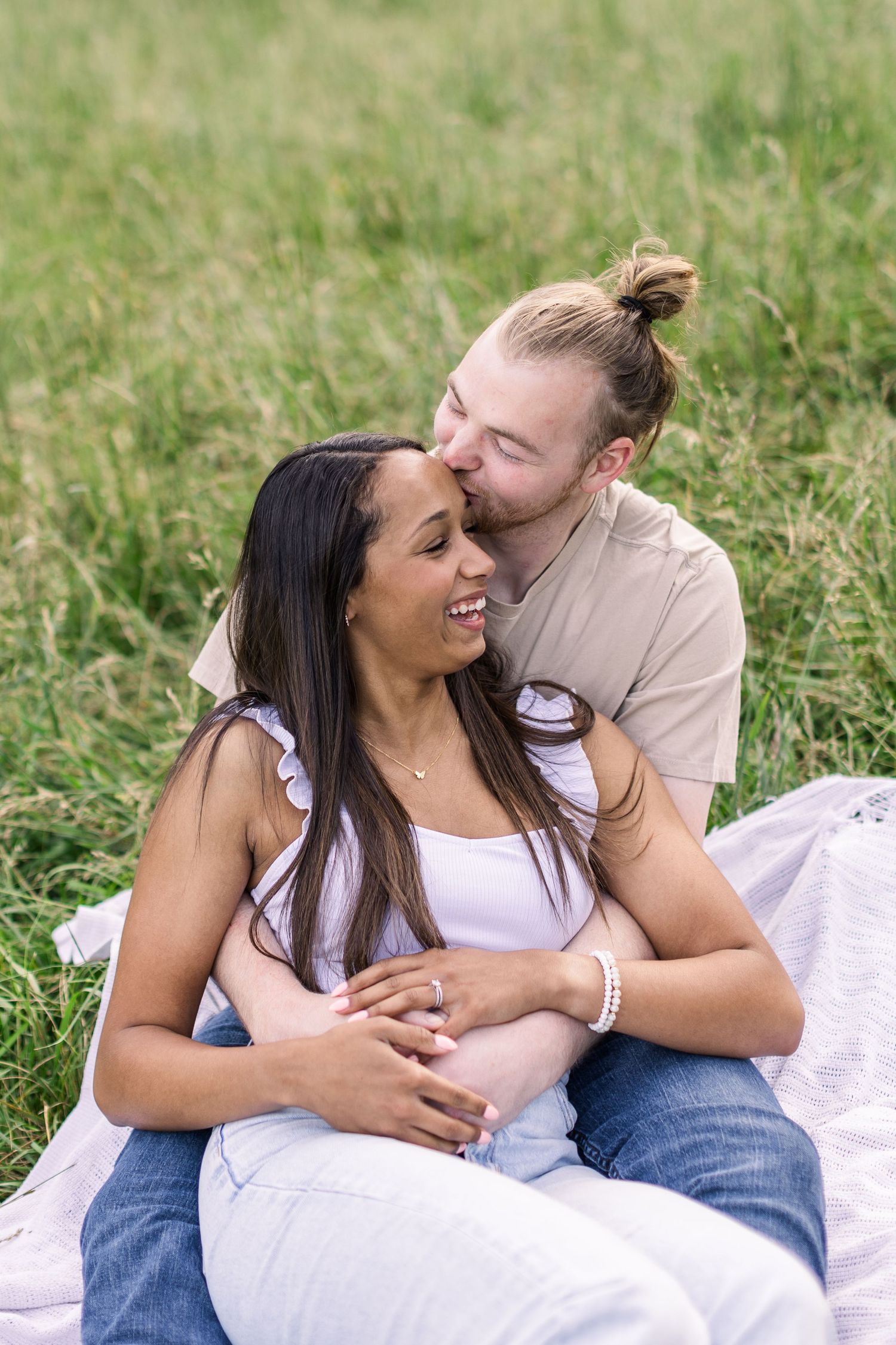A couple shares a tender moment while sitting on a blanket in a sunny meadow.