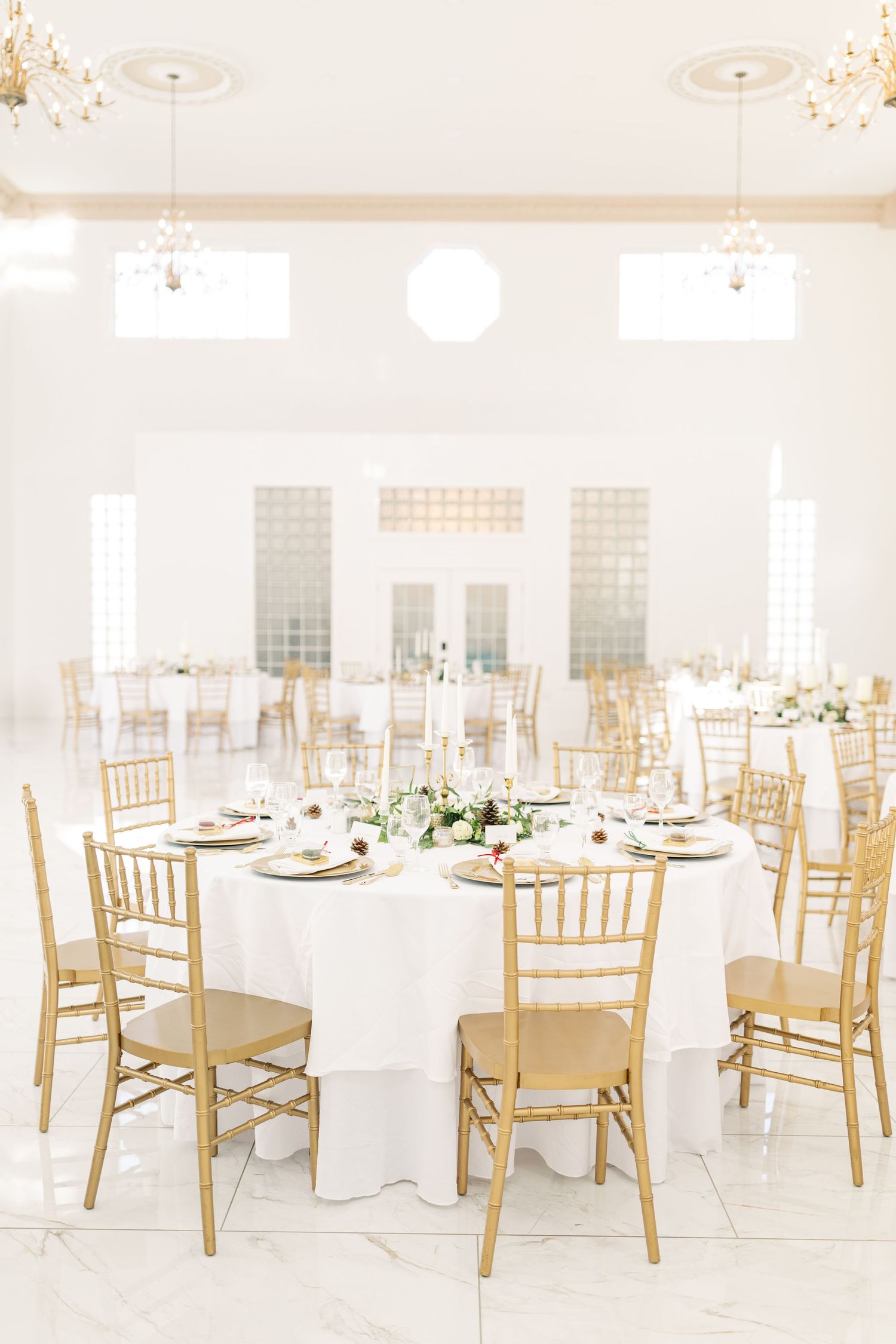 Elegant white and gold wedding reception venue with round tables and chiavari chairs.