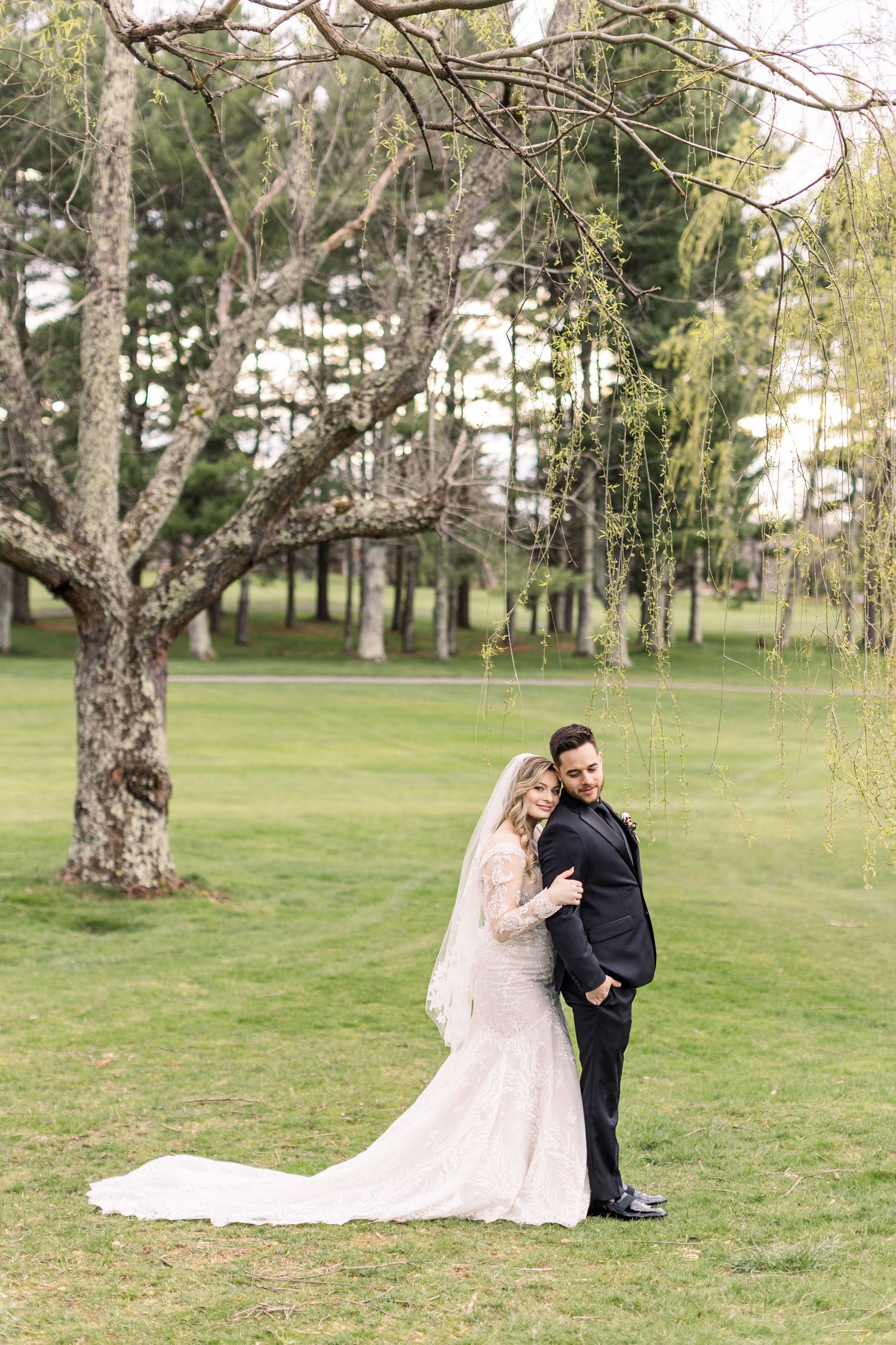 A romantic wedding portrait under a weeping willow tree in a park setting.