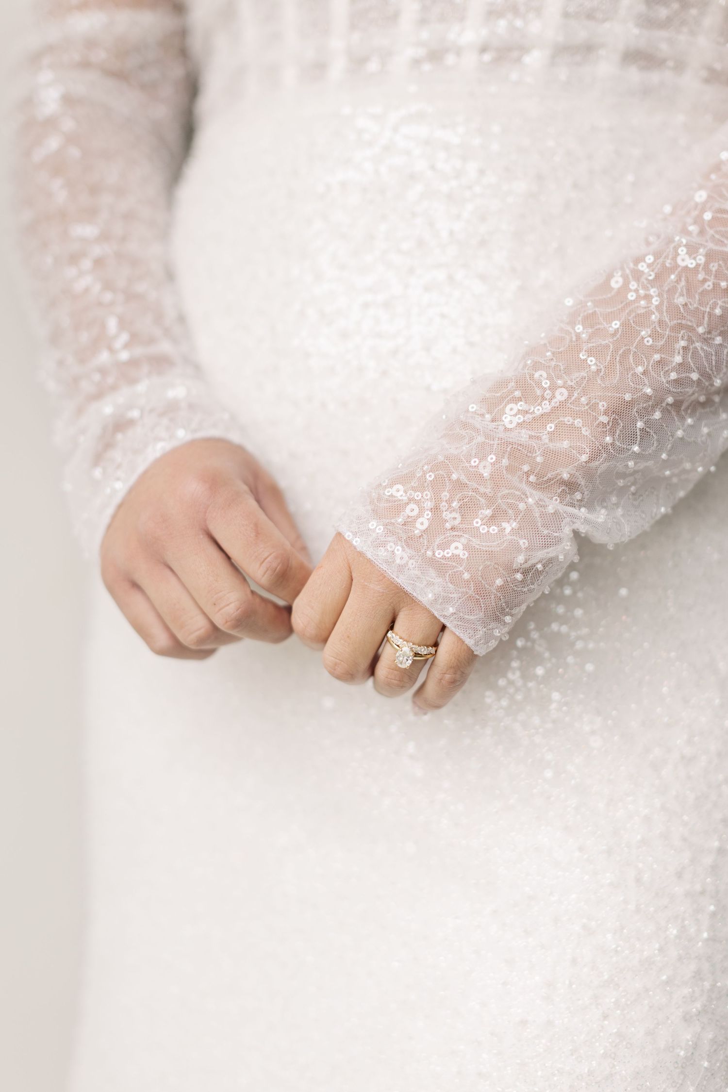 Close-up of delicate lace wedding dress sleeve with engagement ring on hand.