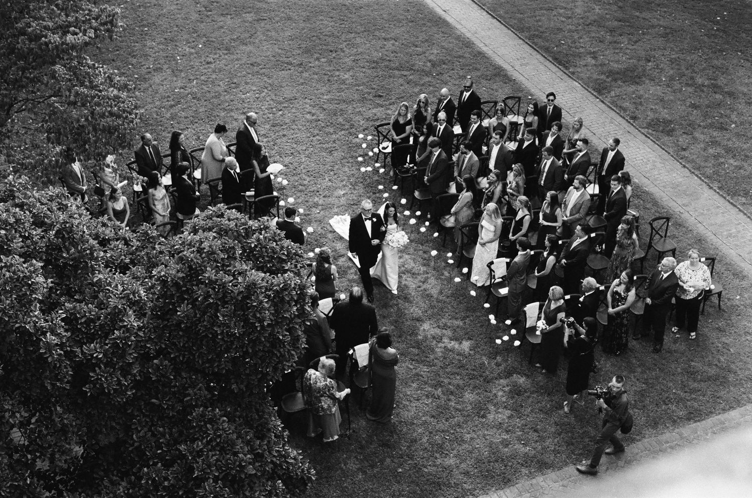 Aerial black and white view of outdoor wedding ceremony on green lawn with guests.