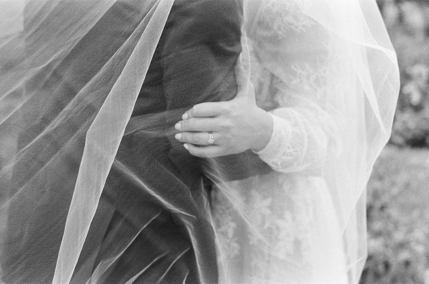 Black and white close-up of bride and groom embracing under flowing wedding veil.