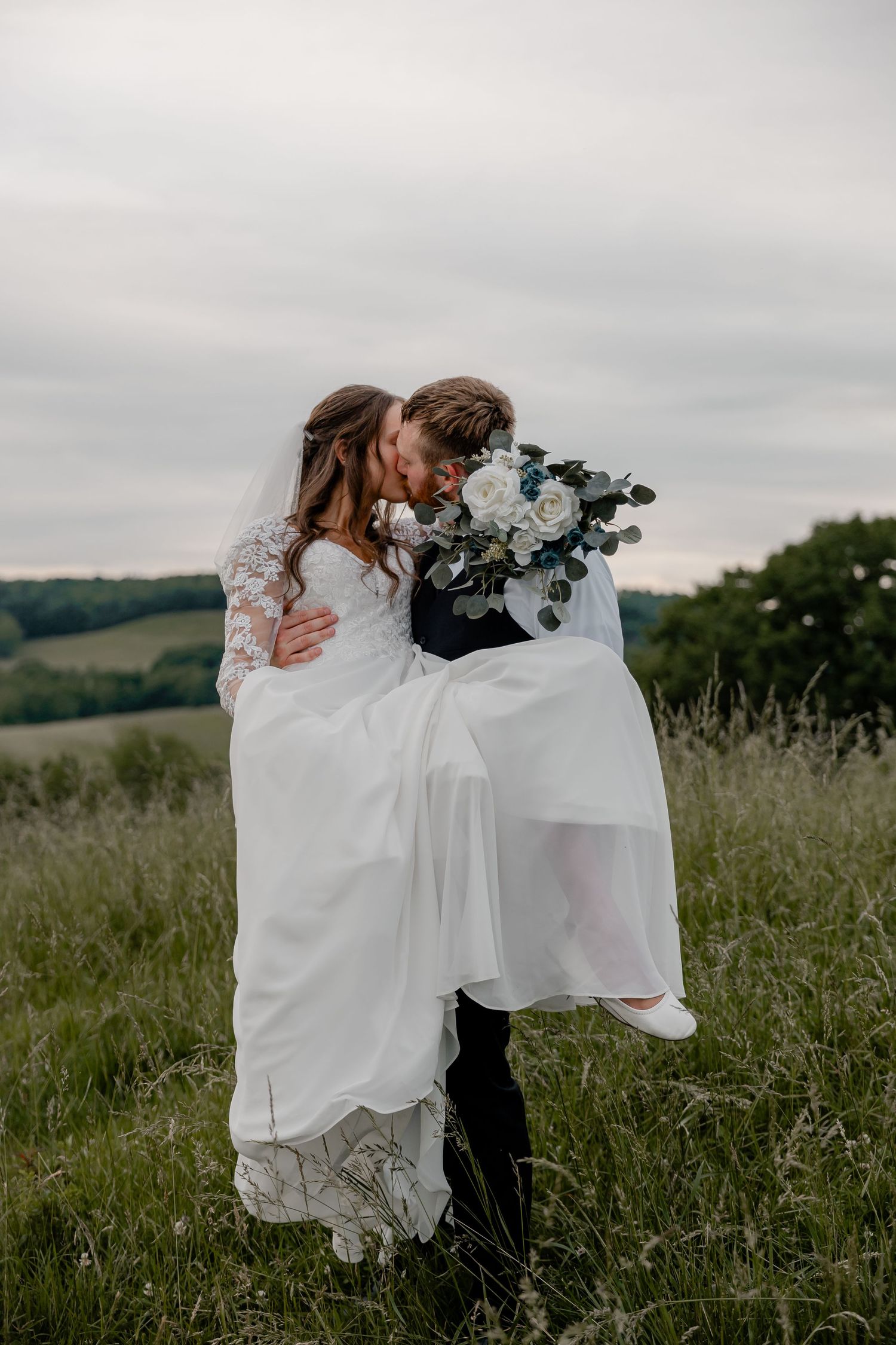 Groom carrying bride through sunset field, sharing kiss as her long wedding dress flows – Pittsburgh wedding photography.