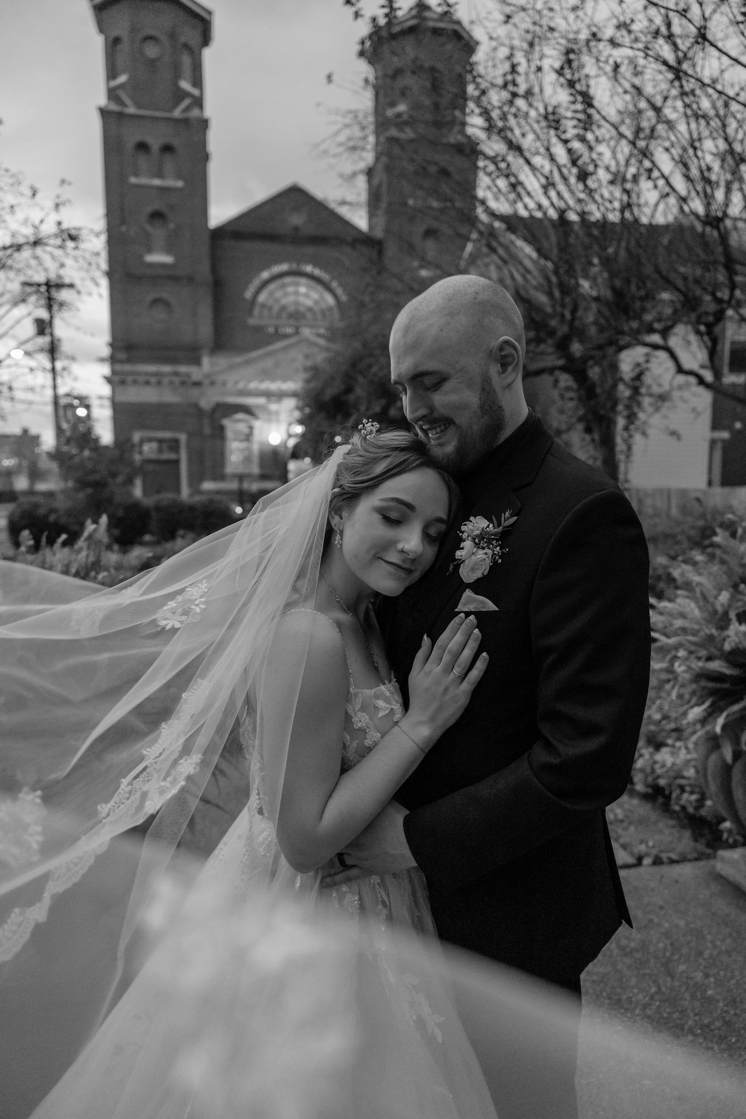 Bride and groom embracing outside Pittsburgh's Grand Priory at dusk, with flowing veil and romantic expressions