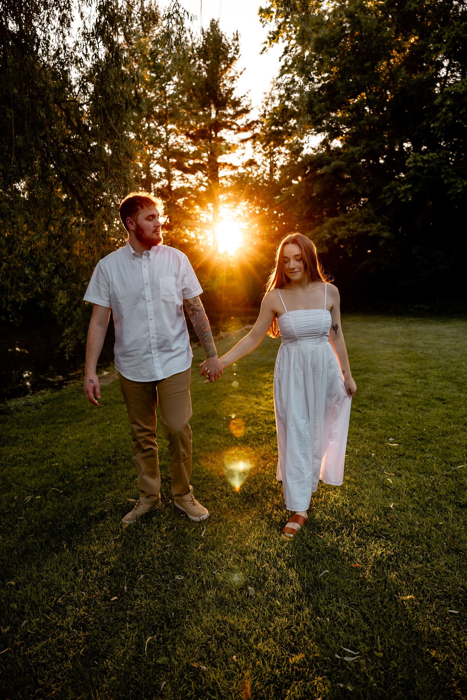 Engaged couple holding hands walking toward camera at sunset with golden light shining through trees – romantic Pittsburgh session.