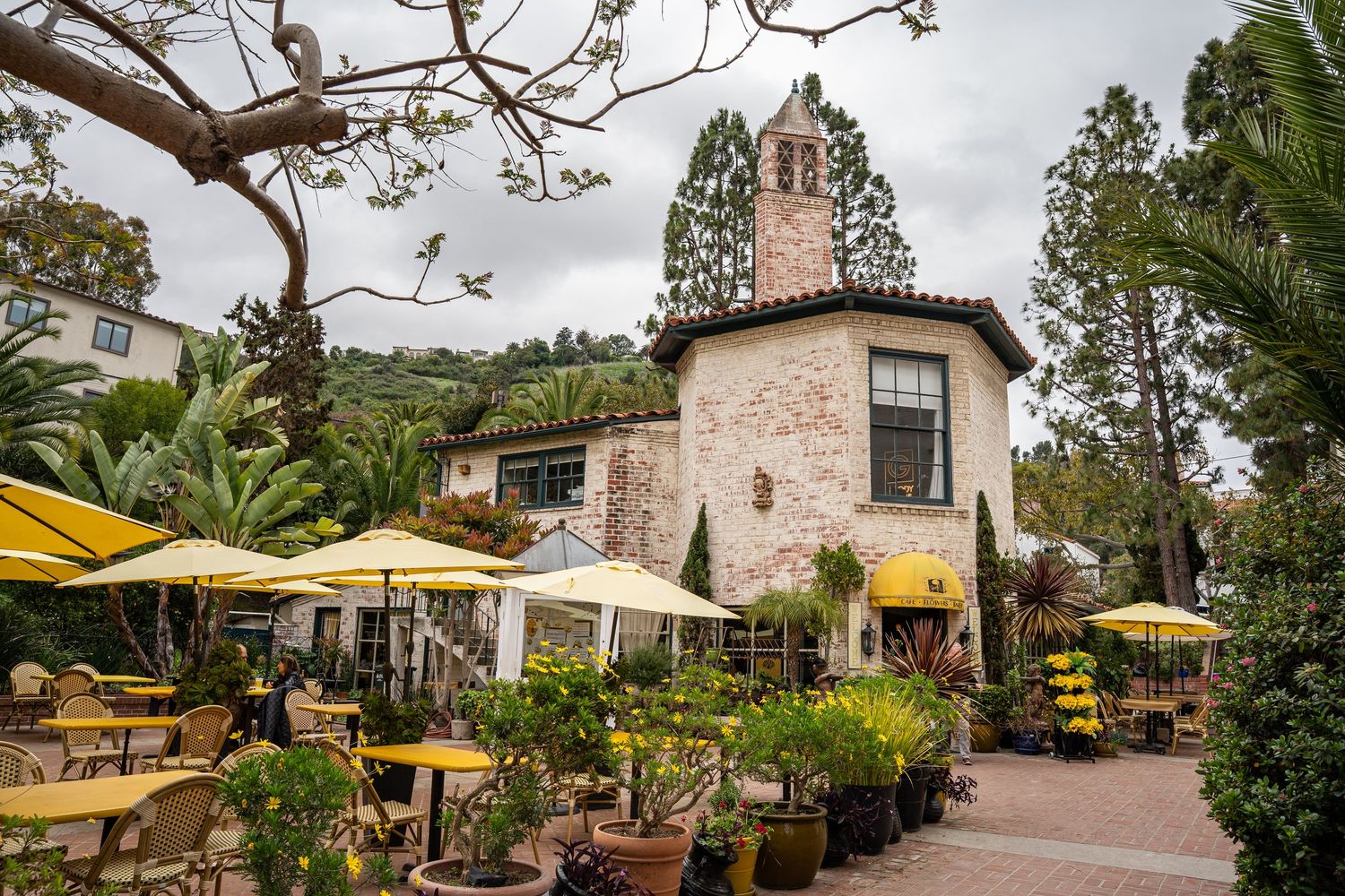 The Yellow Vase restaurant in Malaga Cove. Yellow umbrellas are set up over wooden tables. The brick building is old with a tower.