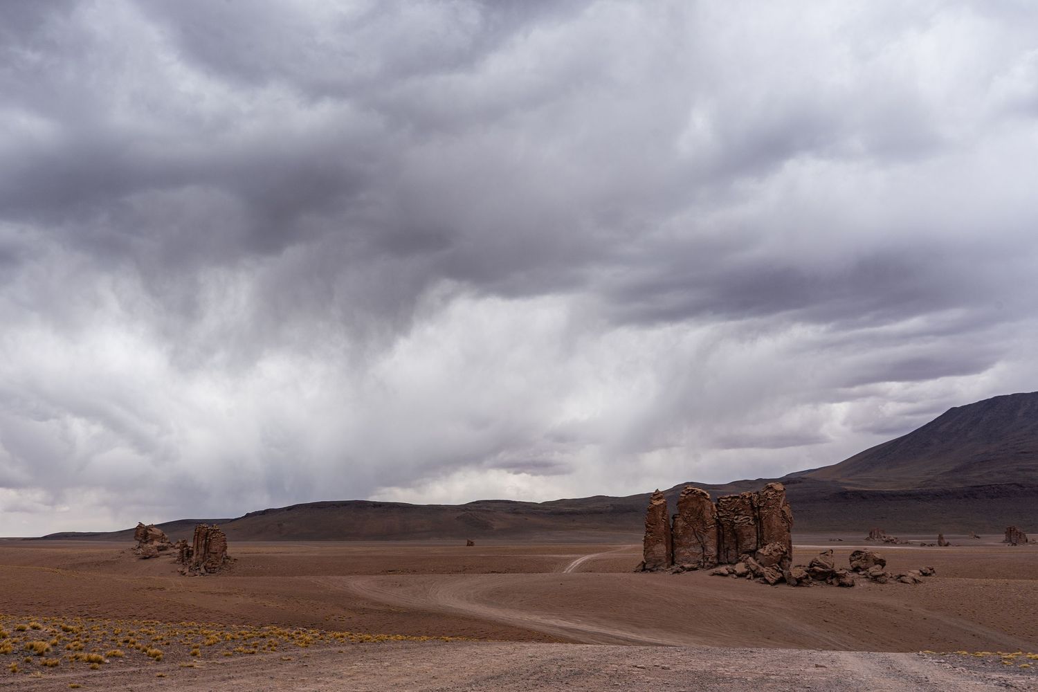 Foreboding storm clouds gather over the desert near San Pedro de Atacama, Chile. A road winds amongst towering rocks.