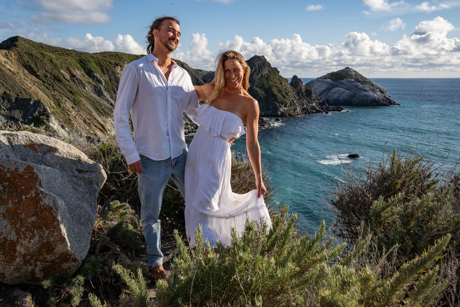 An eloping couple smiles on their wedding day posed on the cliffs overlooking the Pacific Ocean in Big Sur, CA.