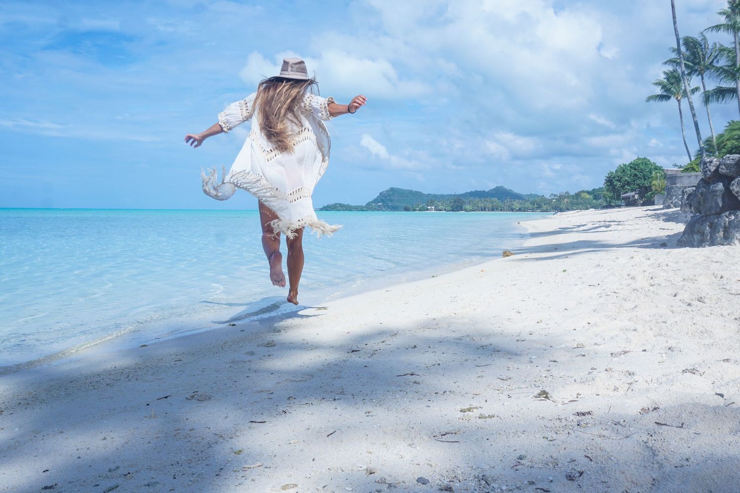 Bora Bora elopement. Stunning white sand beach with palm trees and bride running along the shore.