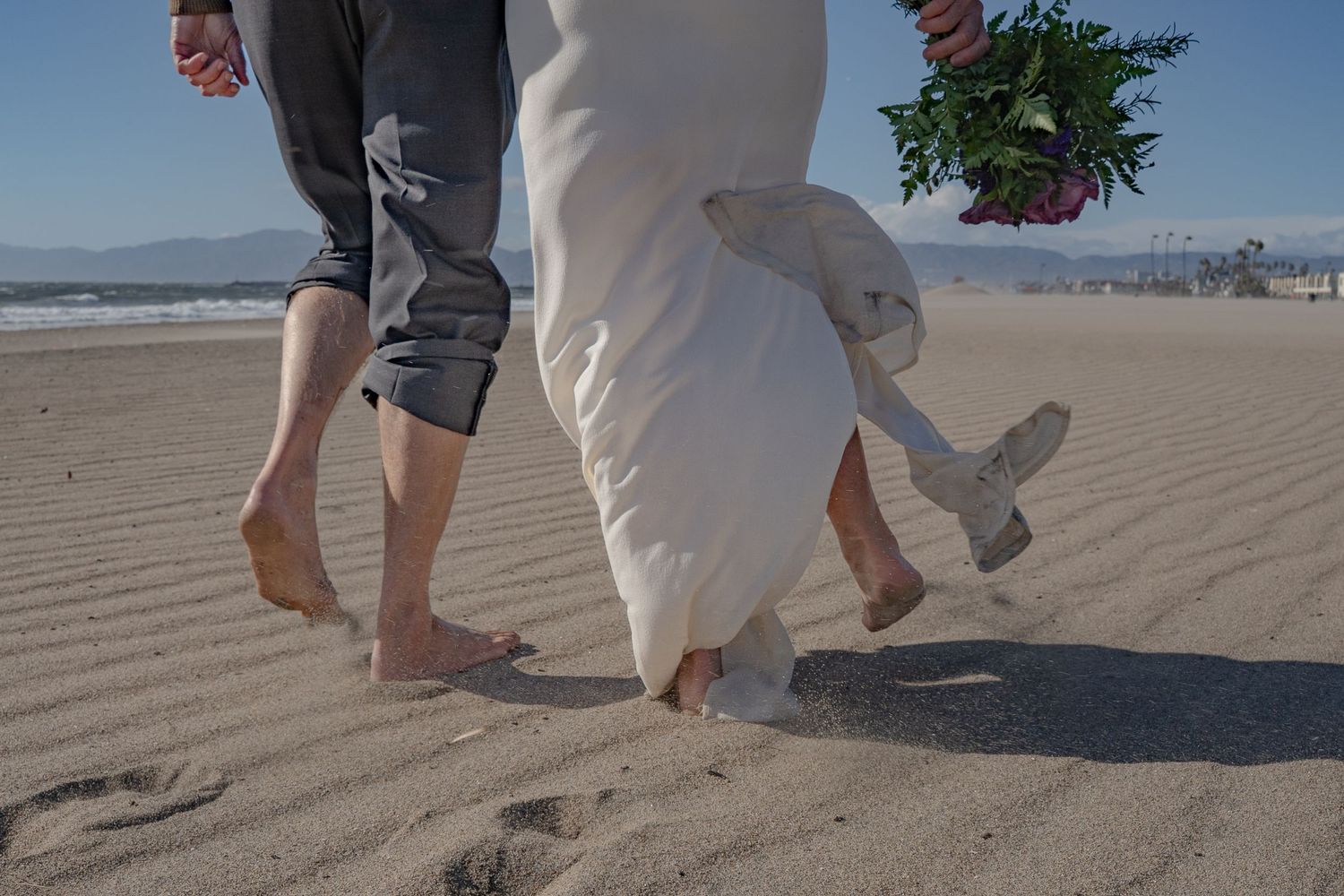 A vow renewal couple walks through a sand storm on the beach in Playa del Rey, Los Angeles, California.