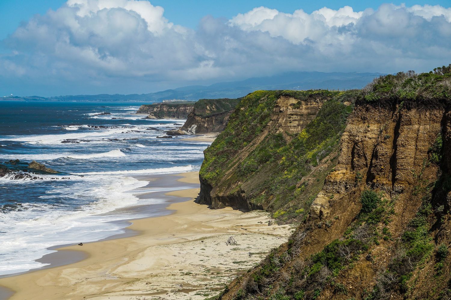 The pacific ocean stretches down a long deserted beach backed by cliffs in California.
