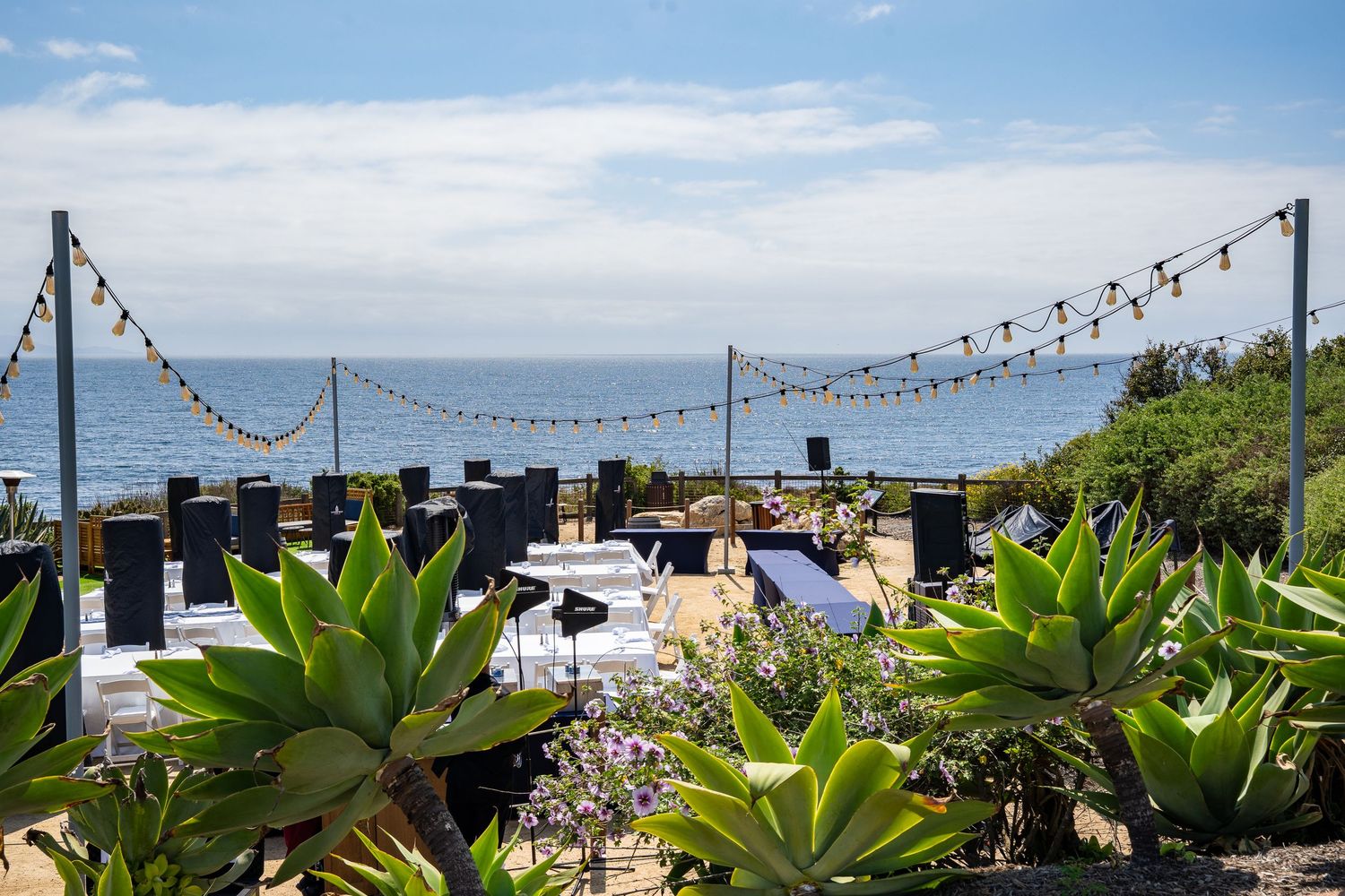An intimate wedding party is being set up on the patio of Terrenea Resort overlooking the Pacific Ocean. It is a beautiful day.